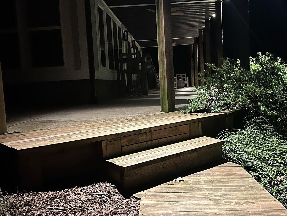 Wooden porch steps leading to a dimly lit deck beside green shrubs at night