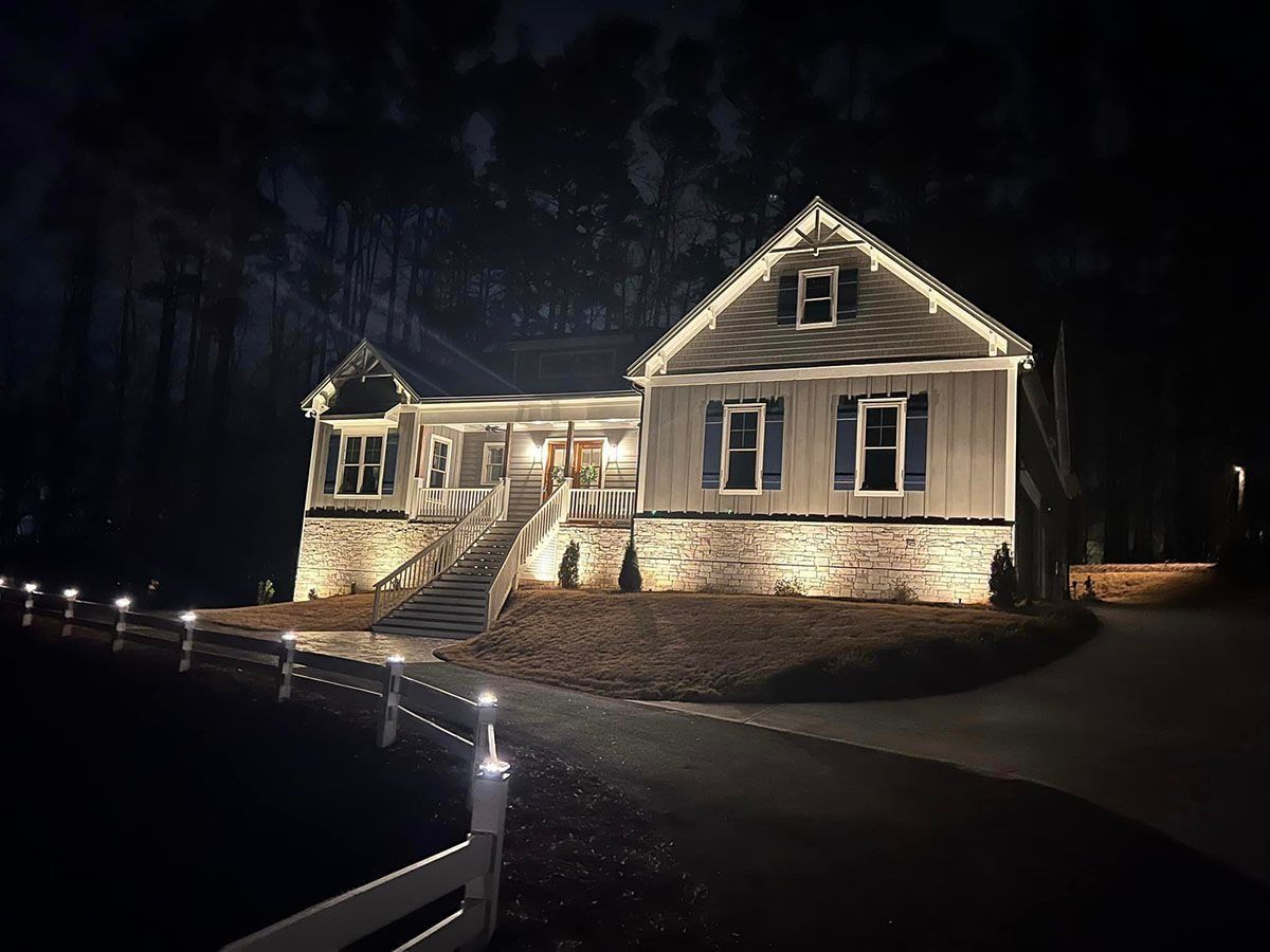 Night-lit house with stone facade and illuminated walkway in a dark wooded setting