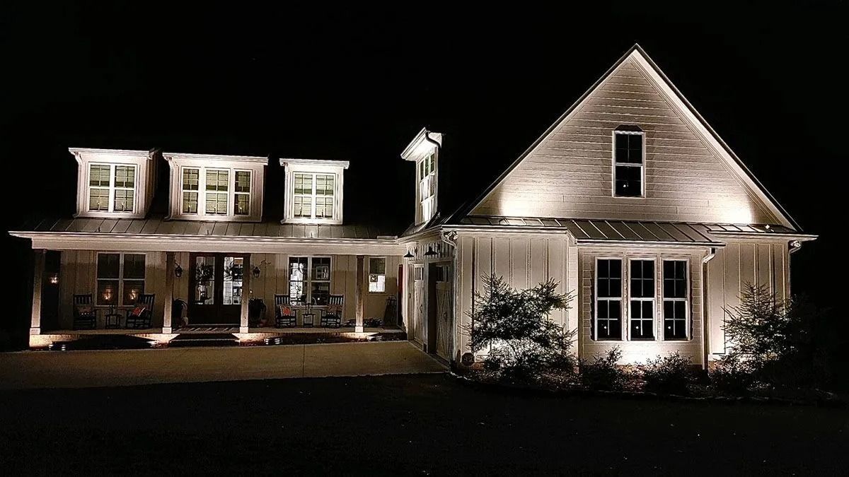 House at night outlined with white holiday lights, with illuminated windows and porch.