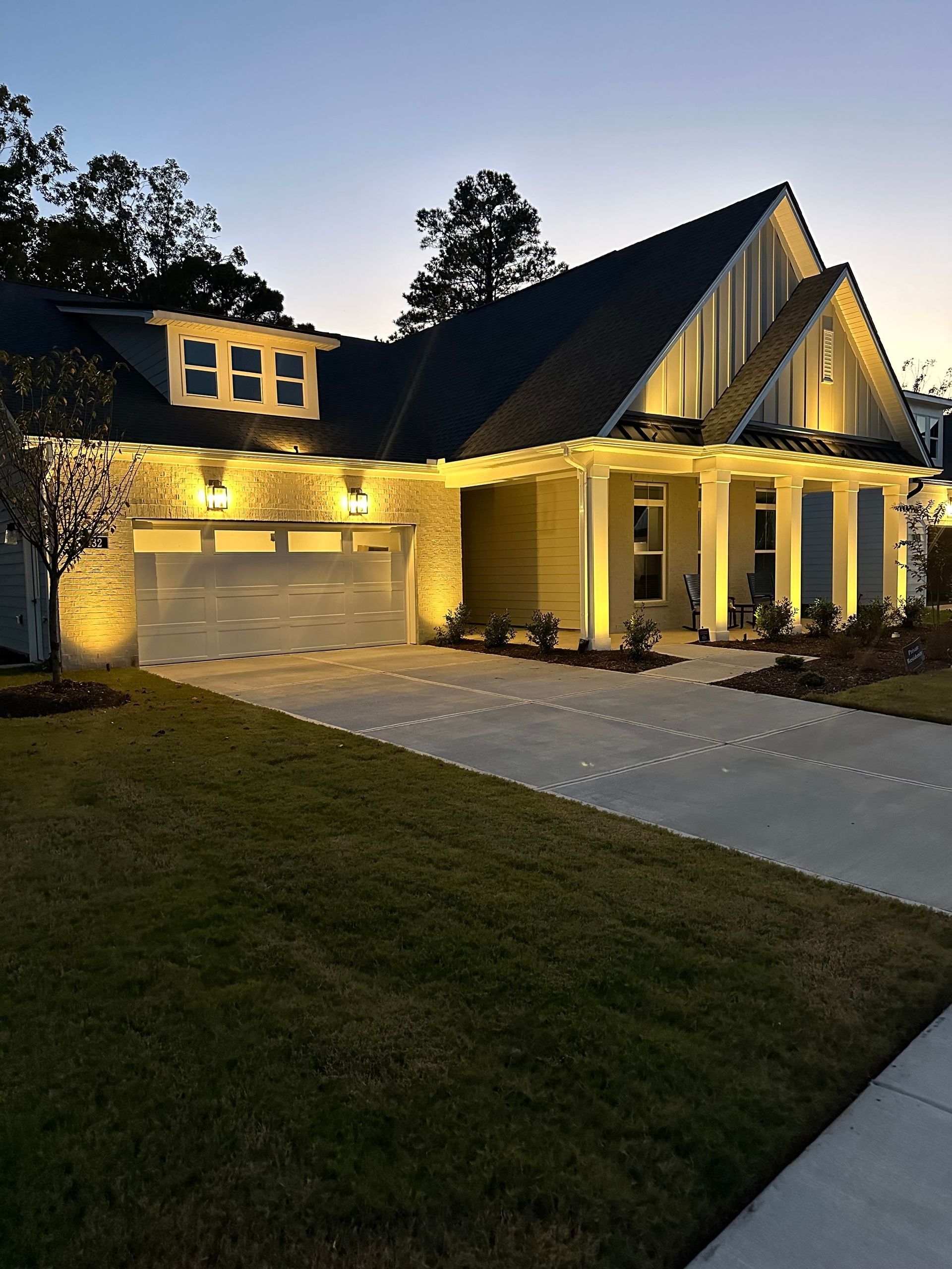 Large two-story house with lit porch and garage at dusk, featuring a steep roof and driveway