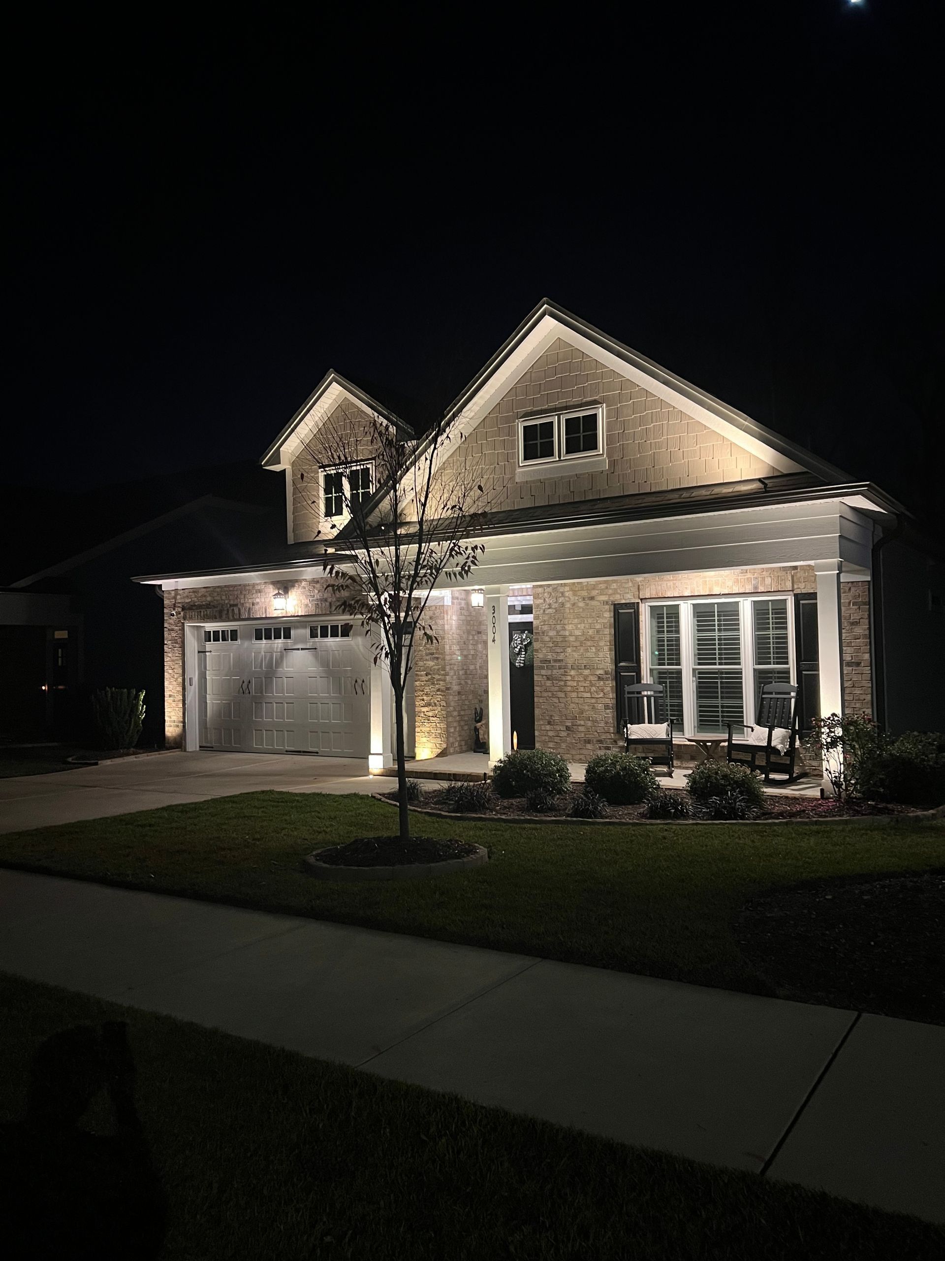 Well-lit suburban house at night with garage, front porch, and lit windows