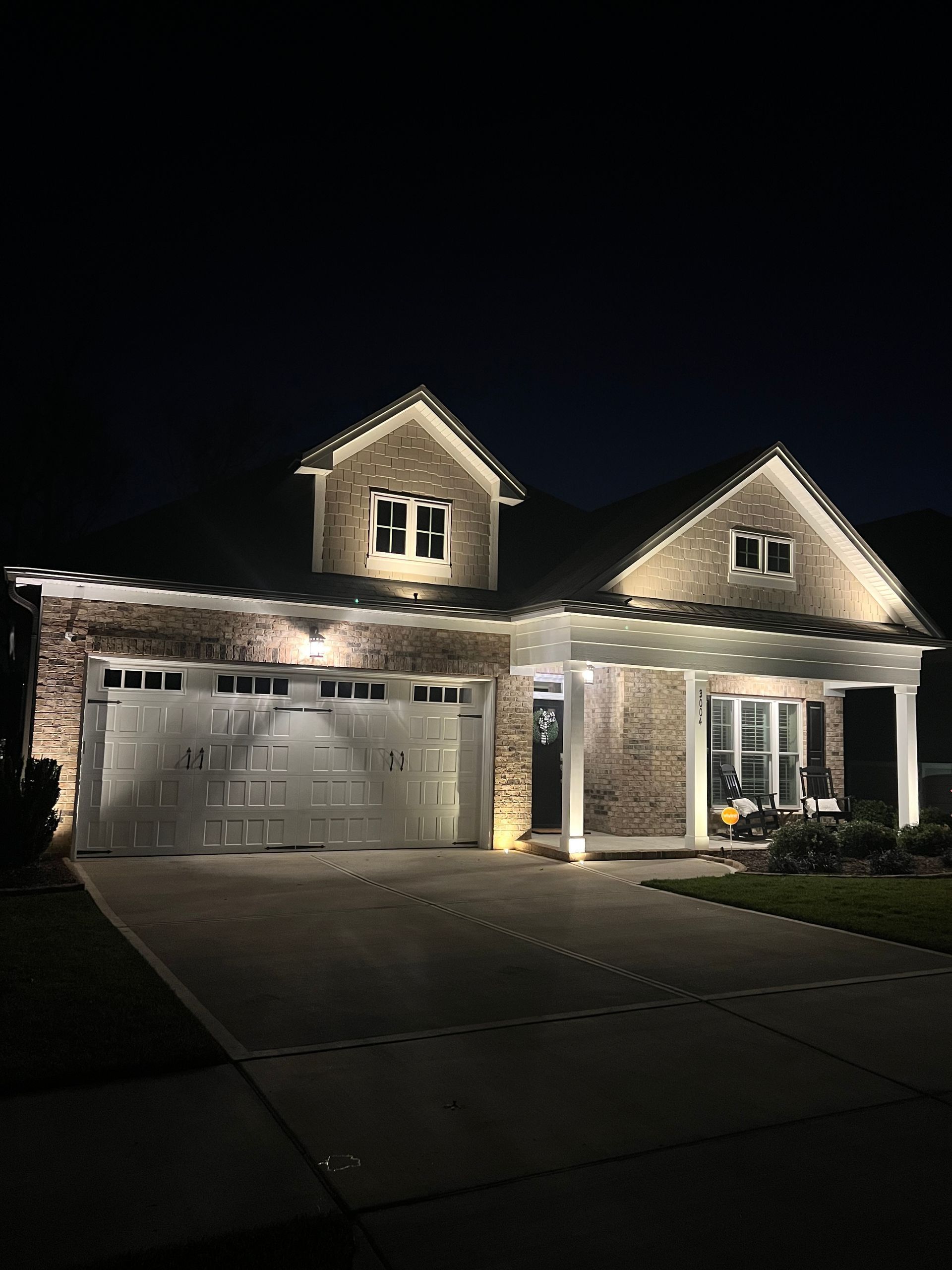 Two-story suburban house at night, lit by exterior lights with a two-car garage and driveway.