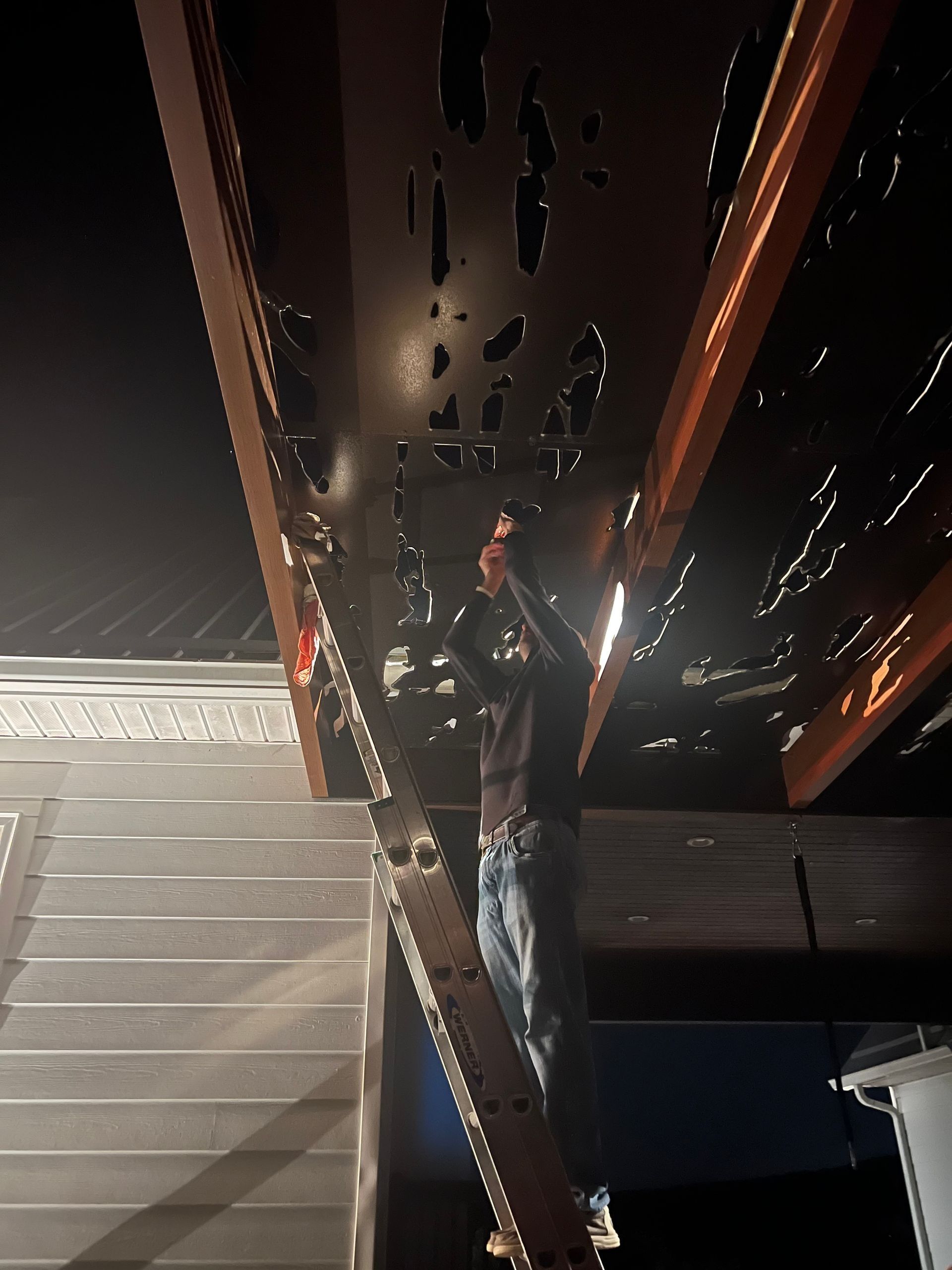 Person standing beneath a dark, reflective structure at night, lit by nearby lights.
