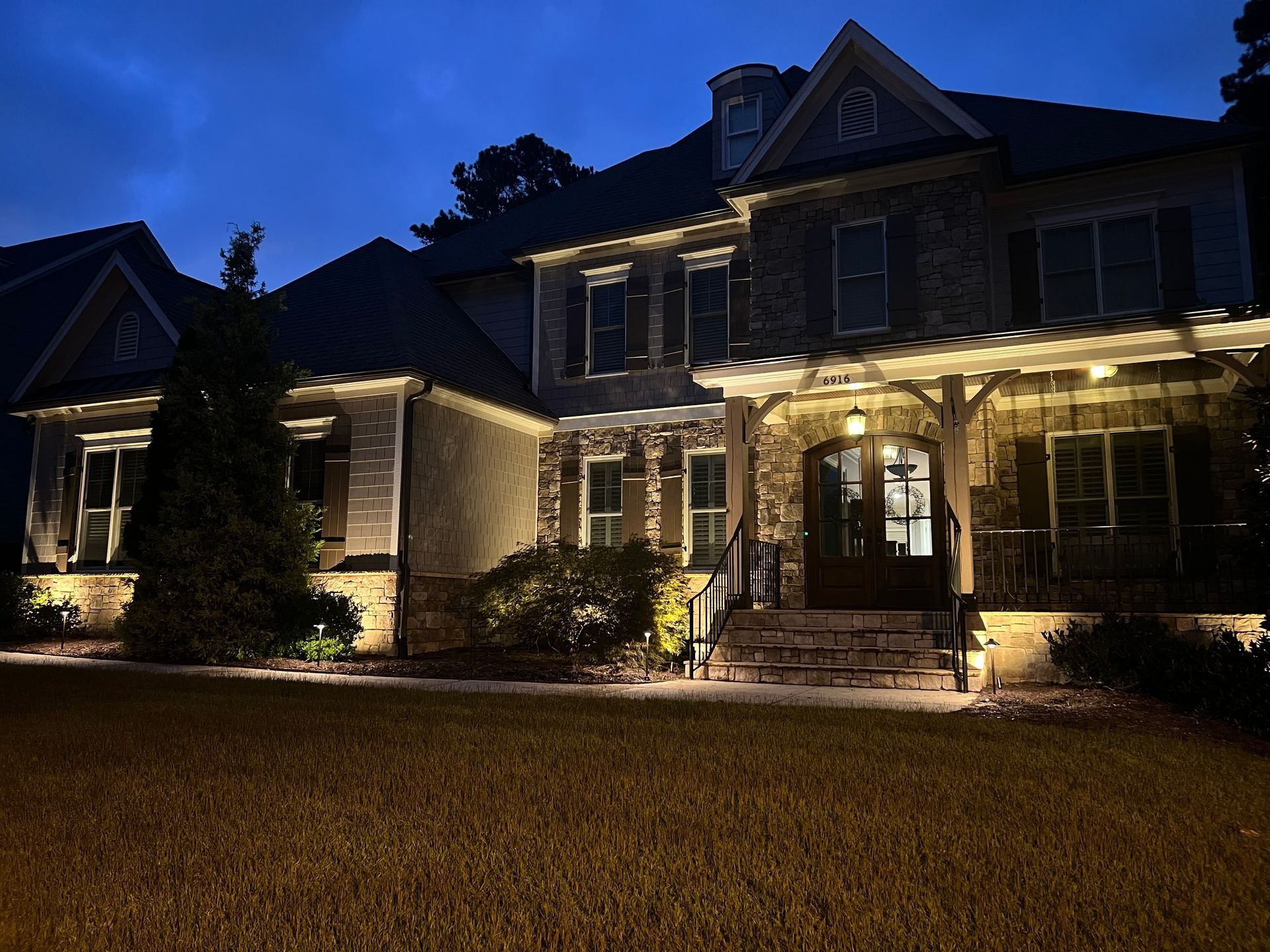 Two-story brick house at night, warmly lit front porch and windows, with a dark lawn in front