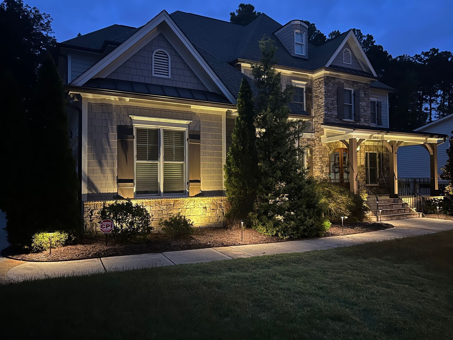 Illuminated stone house at dusk with warm exterior lights and a dark lawn in front