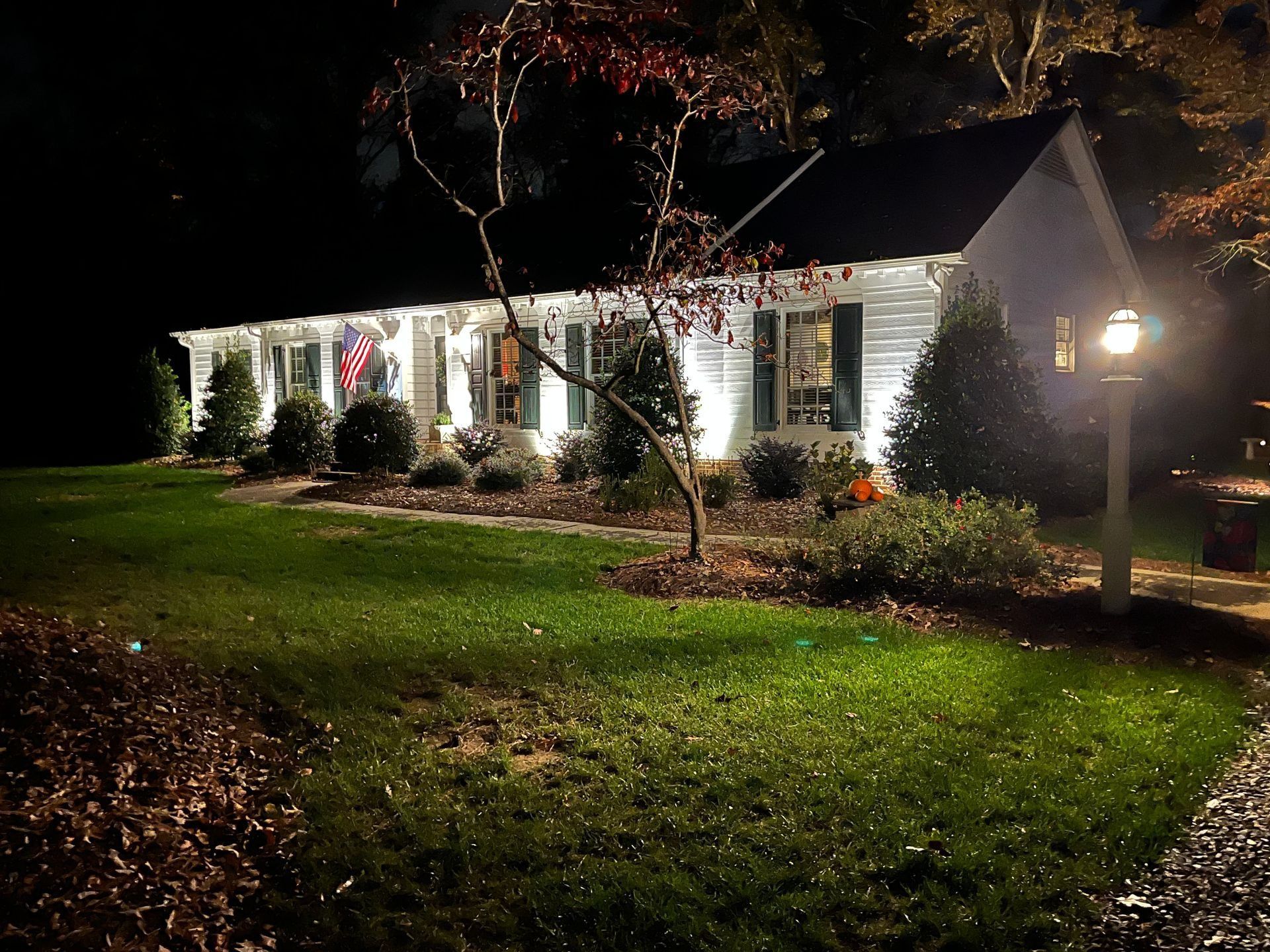 Well-lit white house at night with a front lawn, trees, and porch lights in the dark.