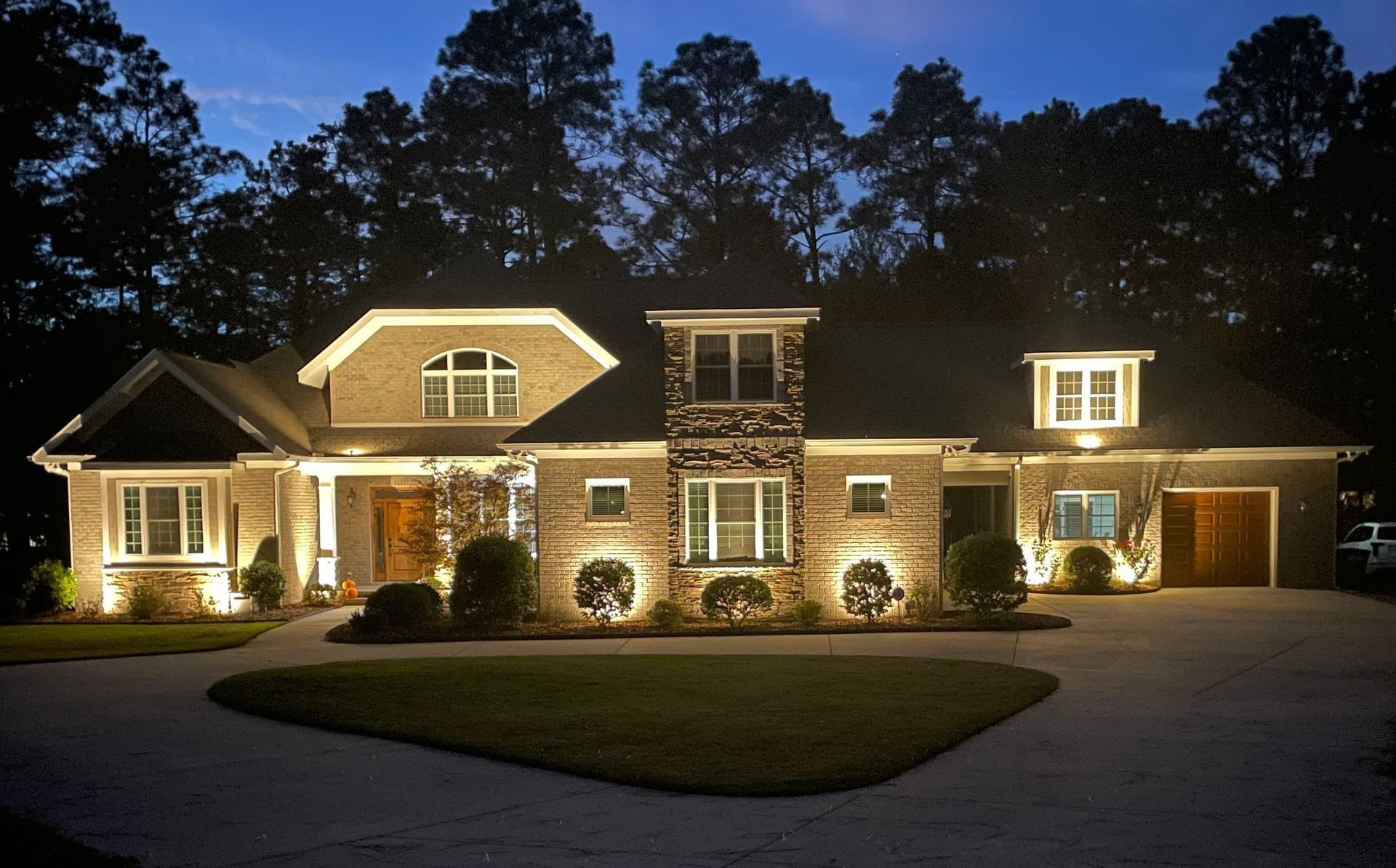 Large, warmly lit brick house at night with a manicured lawn and driveway