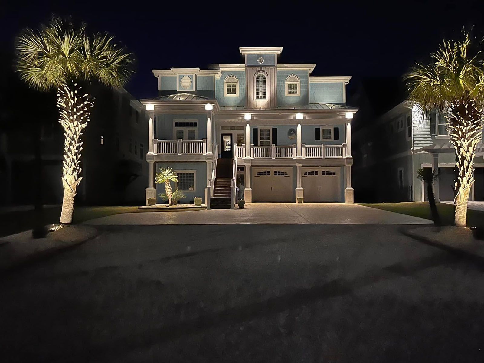 Large illuminated white house at night with palm trees and a dark driveway