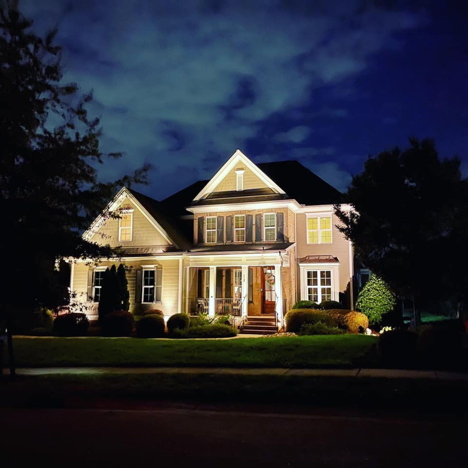 Illuminated two-story house at night with warm porch lights and a dark blue sky
