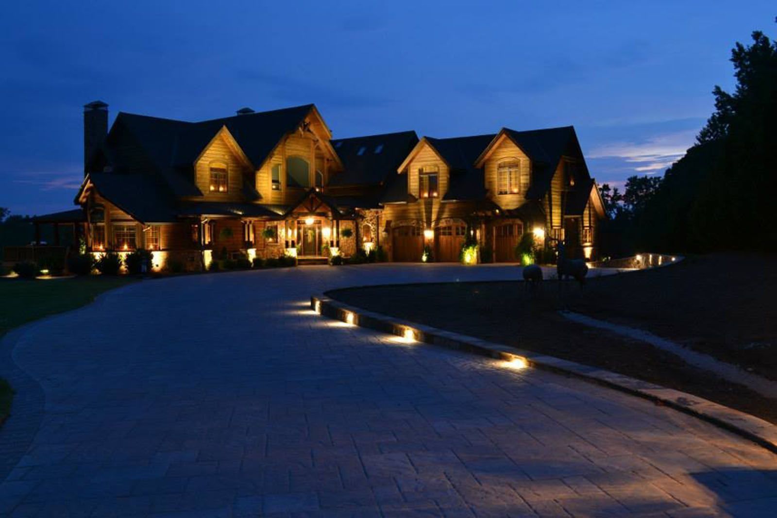 Illuminated stone manor at dusk with warm lights and a curved driveway
