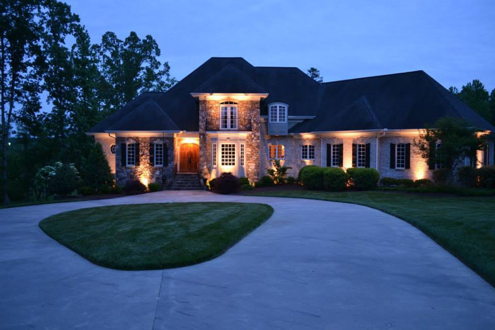 Large brick house lit at dusk, with a curved driveway and manicured lawn.
