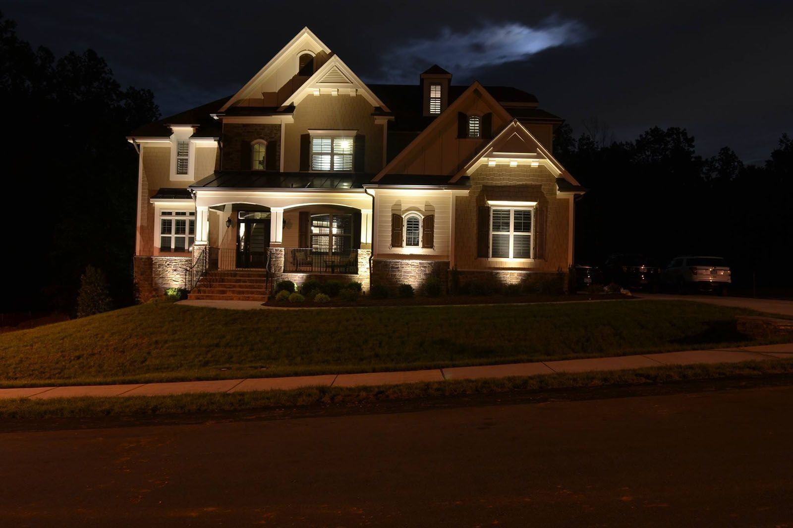 Well-lit two-story house at night with brick facade and steep gabled roof