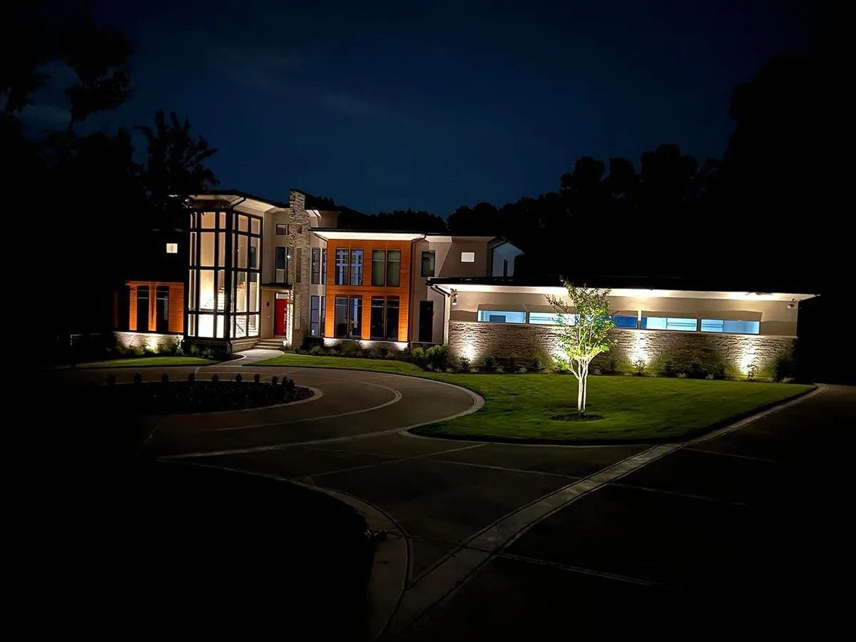 Illuminated modern house at night with curved driveway and landscaped lawn