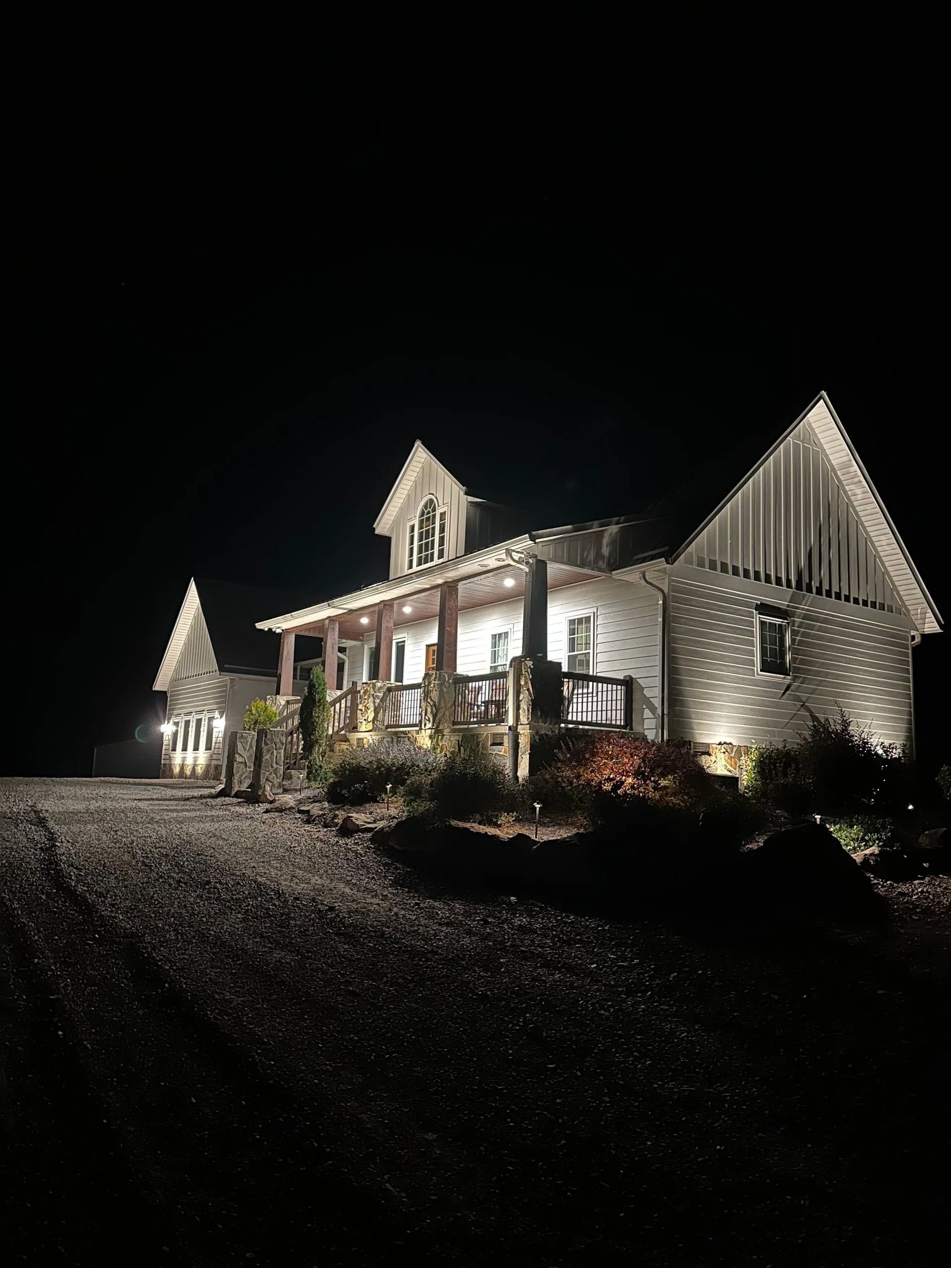 Illuminated white house at night on a gravel driveway, surrounded by darkness.