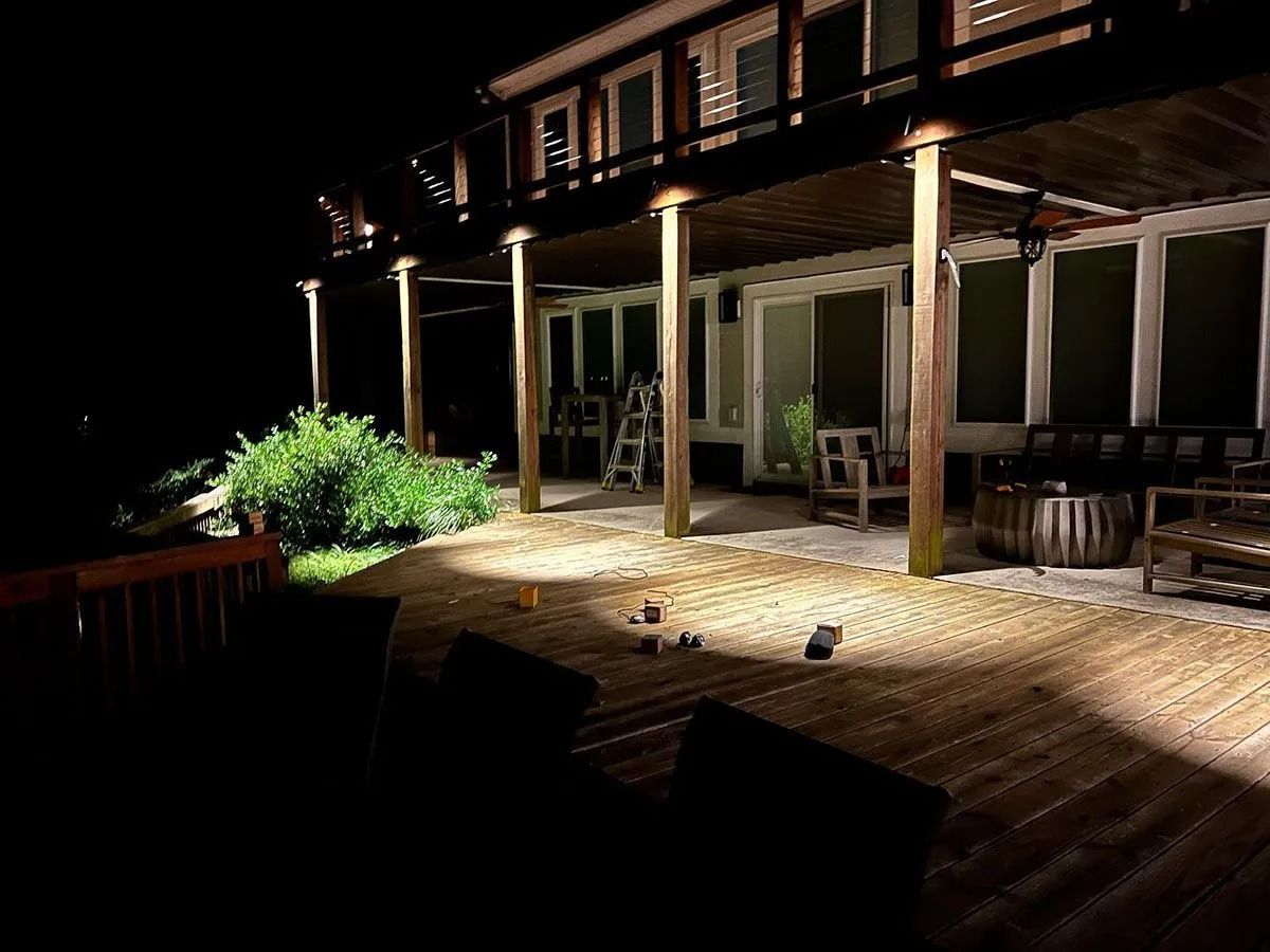 Lit patio with wooden deck, porch lights, and outdoor seating beside a house at night