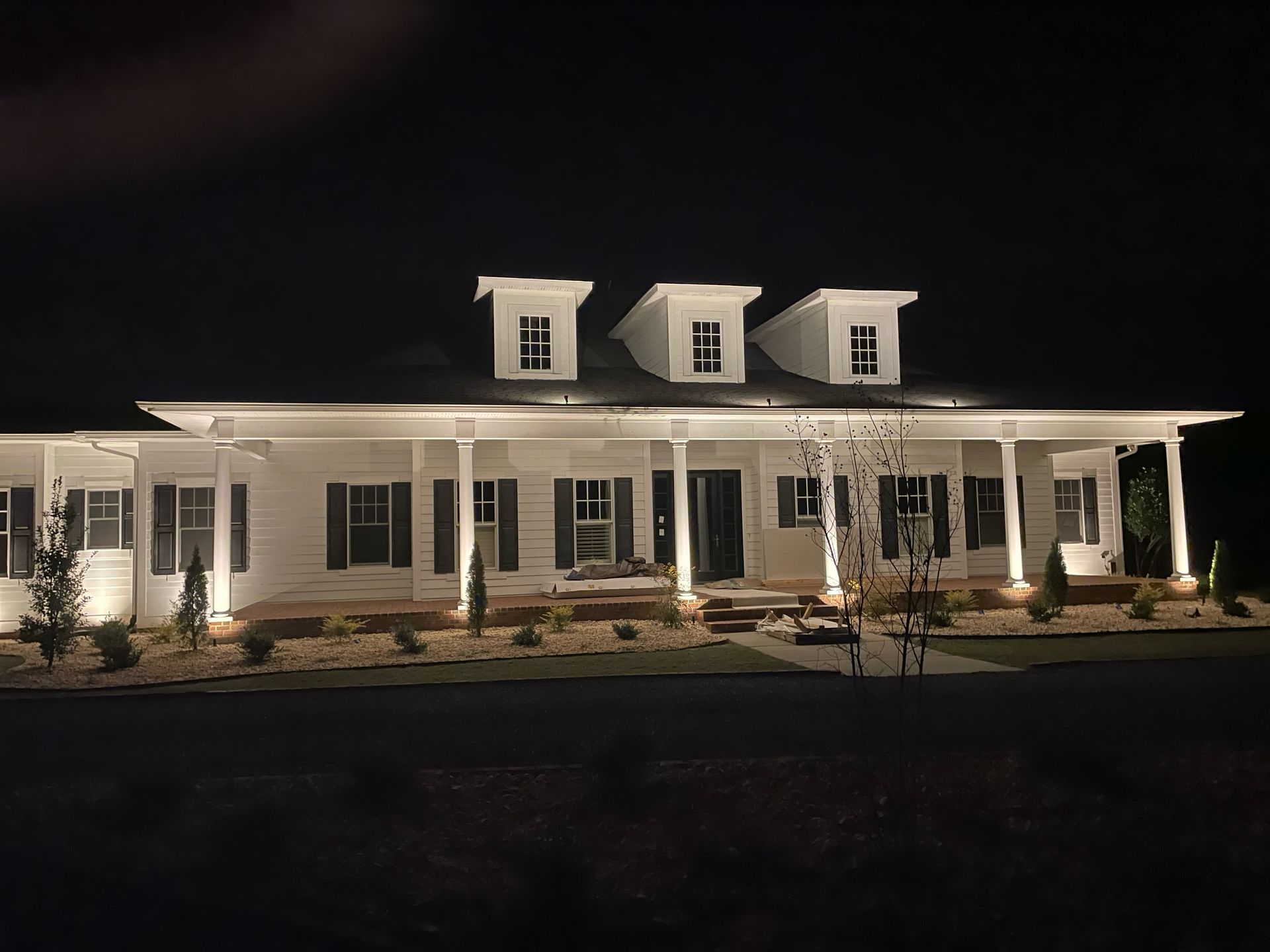 Illuminated white house at night with three dormer windows and a front porch