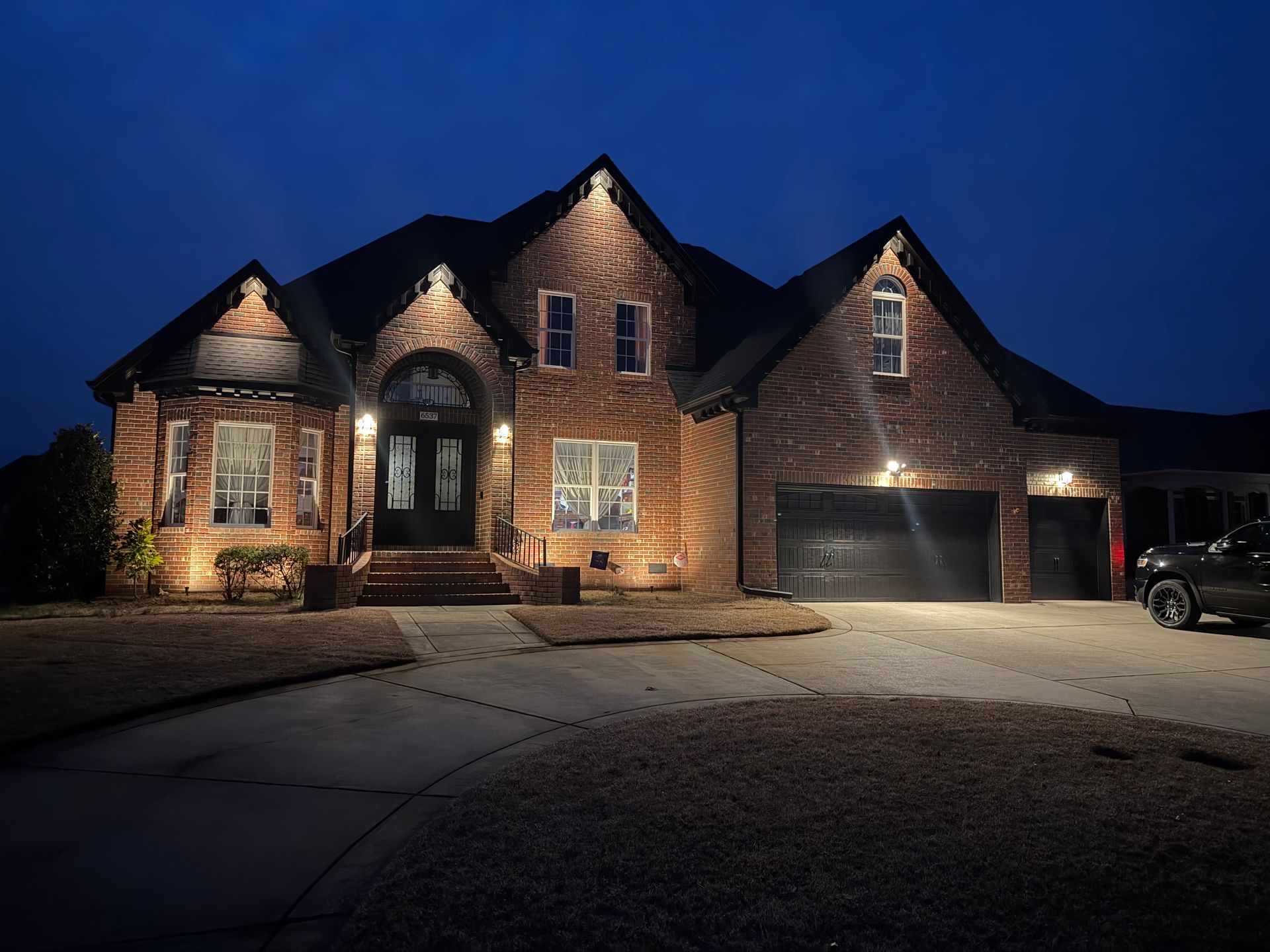 Large brick house with lit windows and garage at night under a dark blue sky