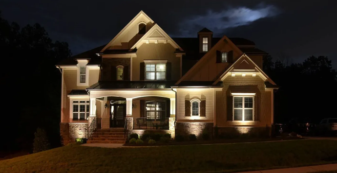 Illuminated large suburban house at night with warm porch lights and dark sky