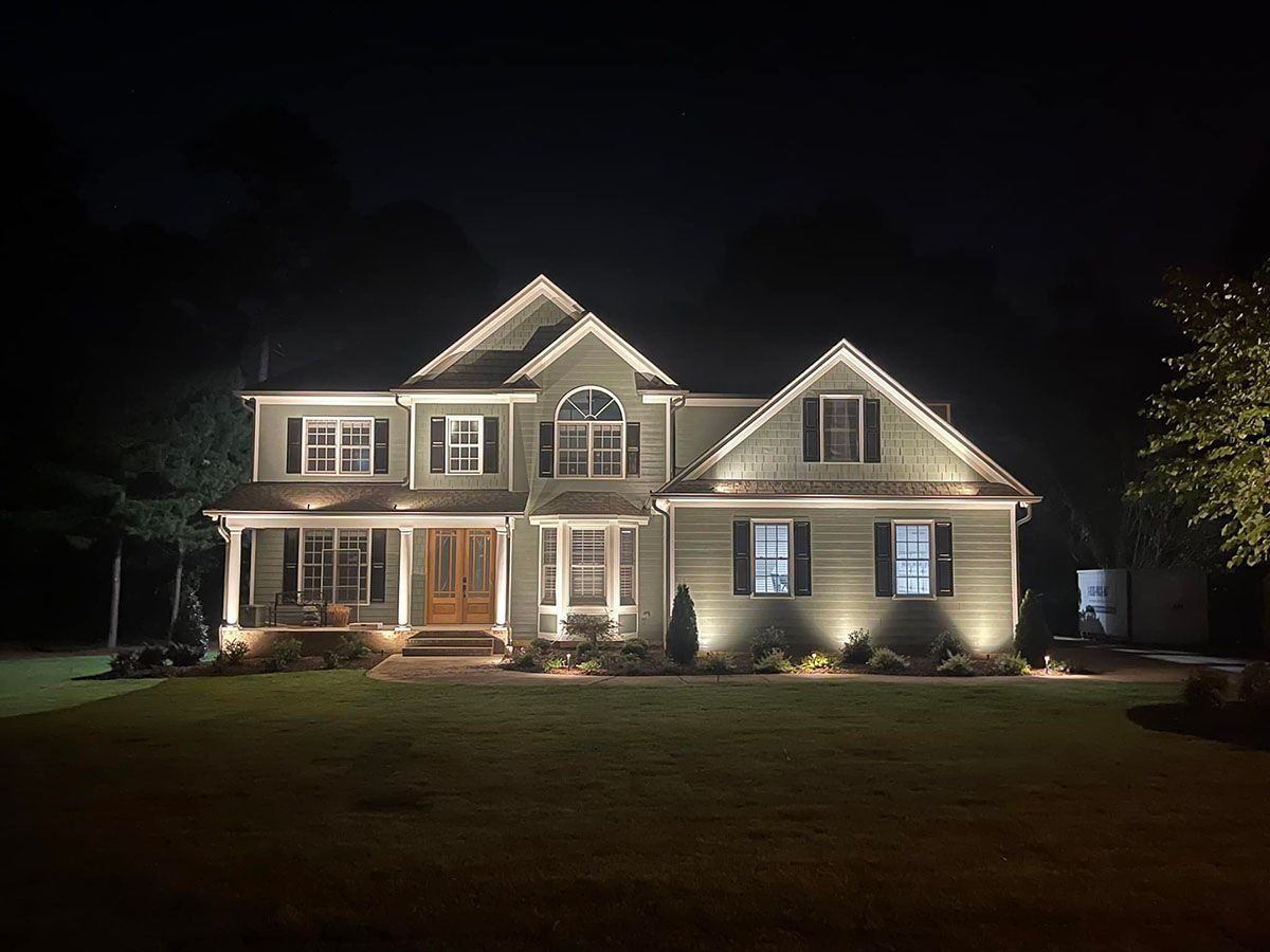 Well-lit two-story suburban house at night with front porch lights and dark lawn