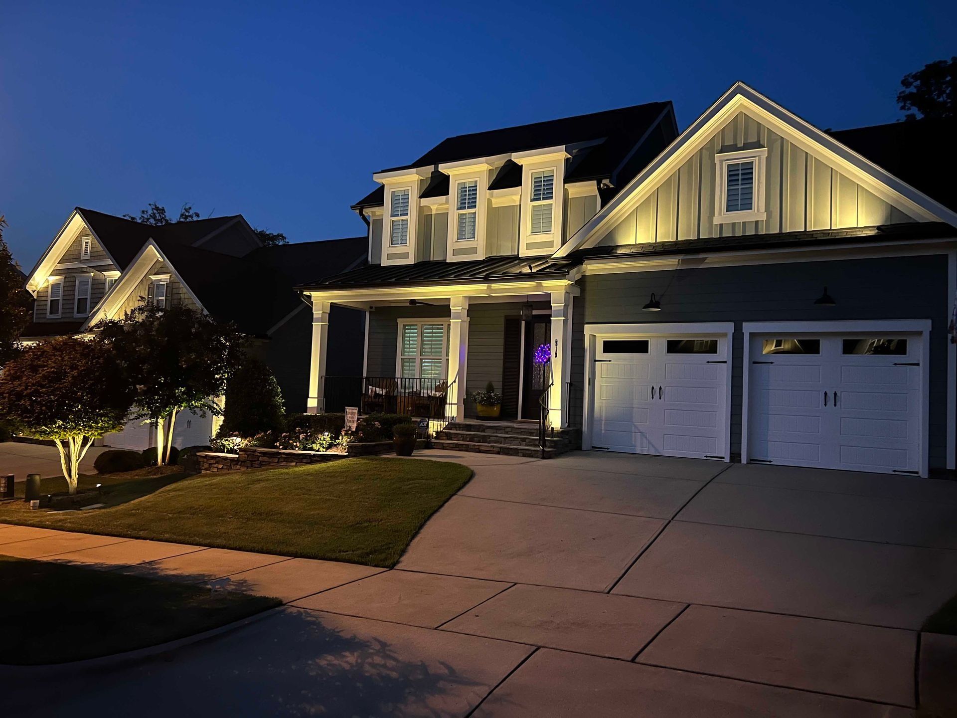 Suburban house at dusk with warm exterior lights, garage, and driveway