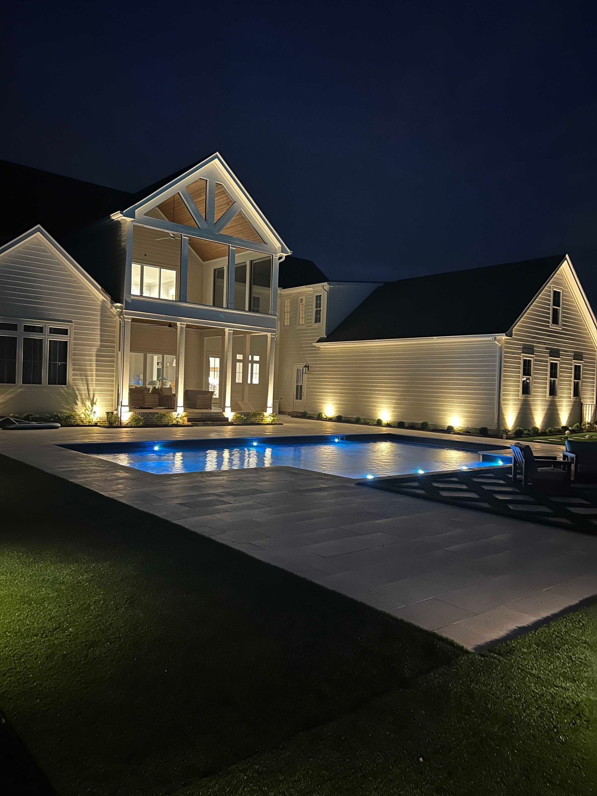 Modern house at night with lit exterior, reflecting pool, and a paved walkway