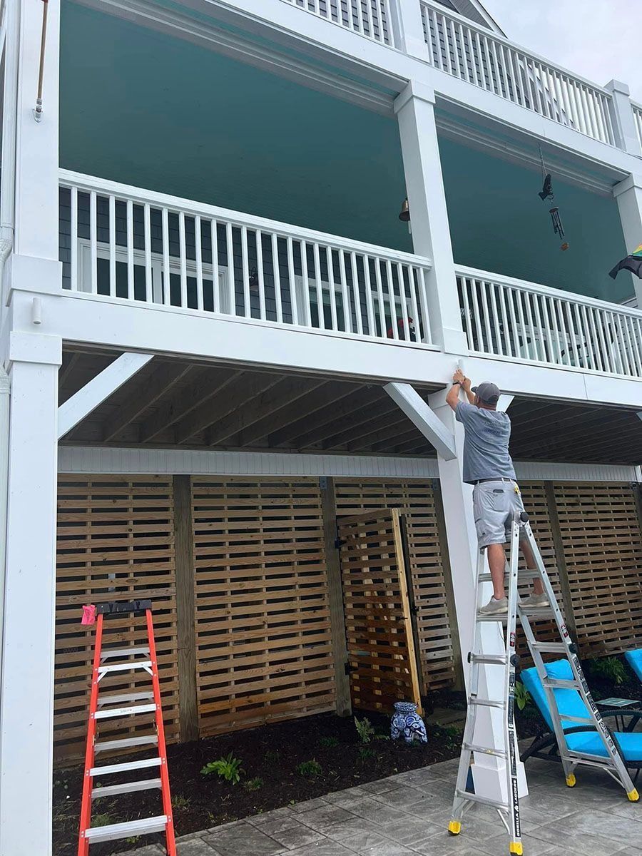 Worker on a ladder painting a white balcony on a two-story house