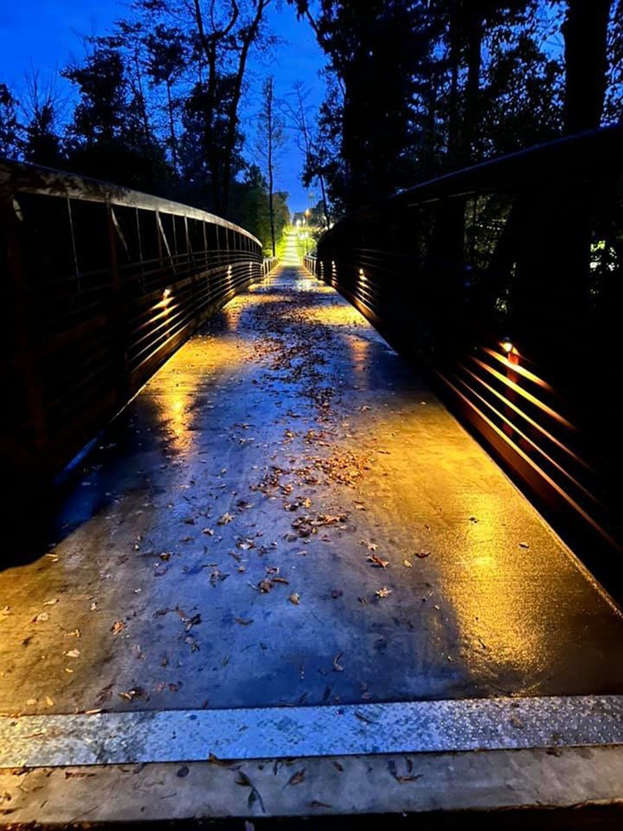Nighttime pedestrian bridge with wet pavement, glowing yellow lights, and silhouetted trees