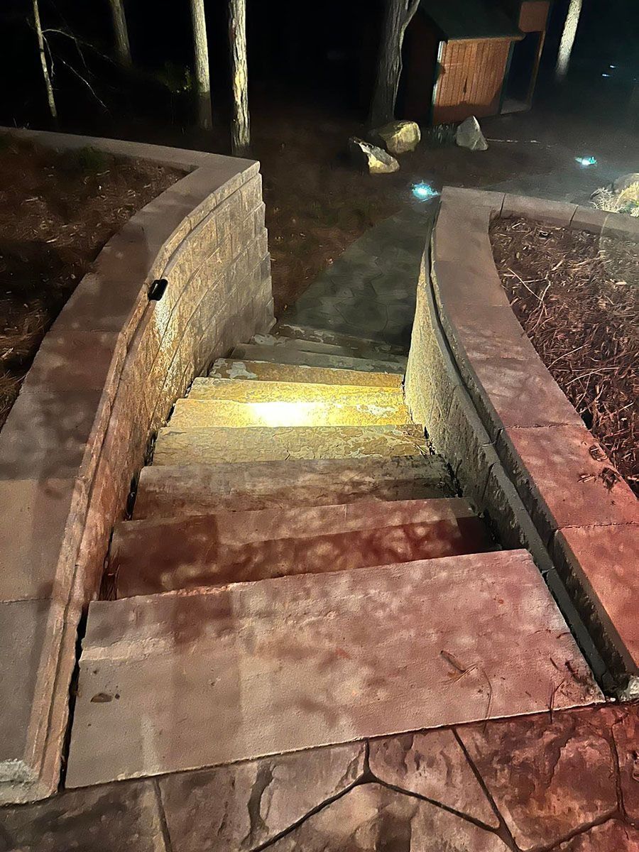 Lit stone stairs descending at night, with low yellow step lights and brick walls on both sides