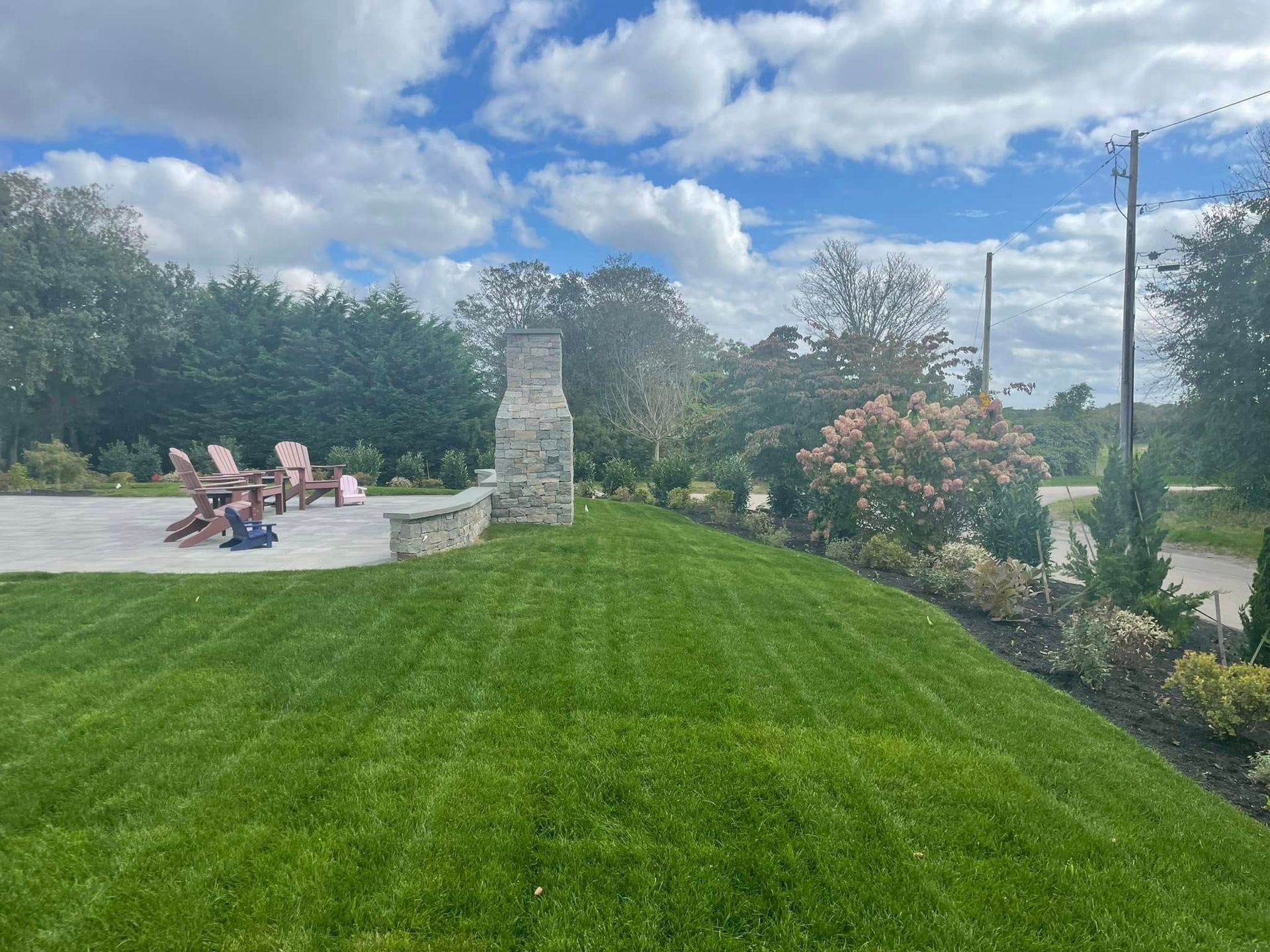 A lush green lawn with a fireplace and chairs in the background.