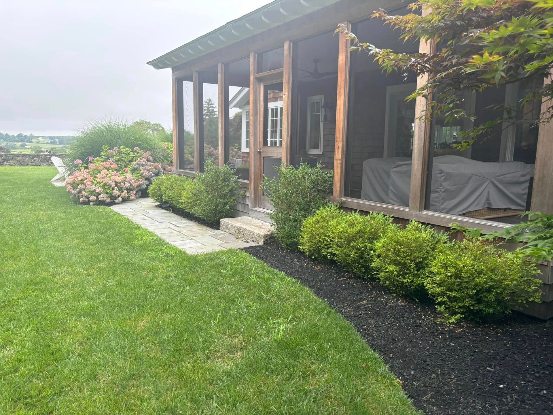 A house with a screened in porch and a large lawn in front of it.
