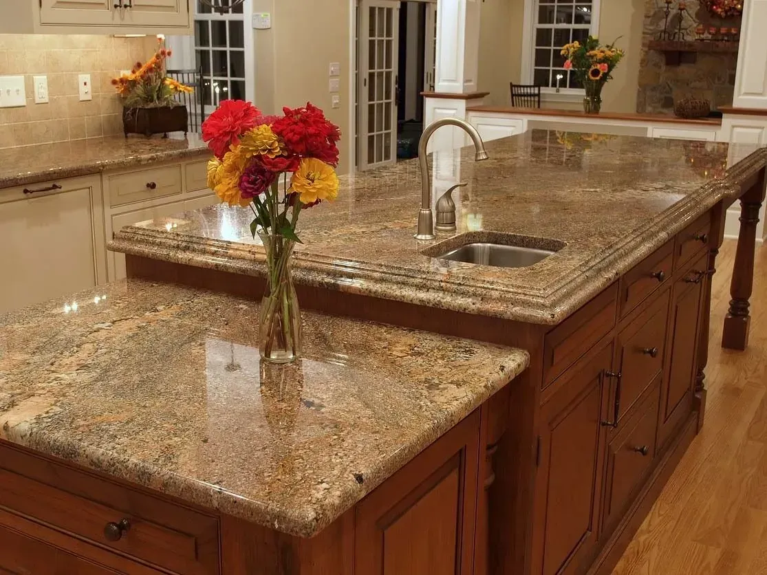 Granite kitchen island with sink and colorful flowers, brown cabinets.