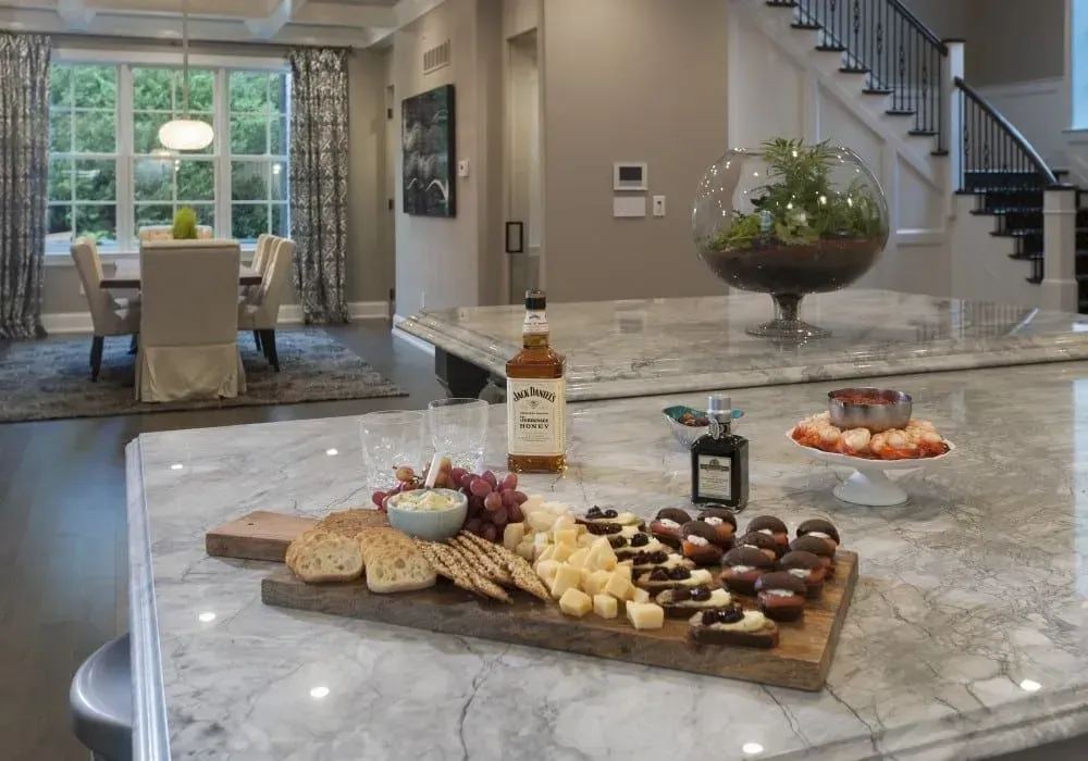 Charcuterie board with snacks and liquor on a marble kitchen island in a modern home.