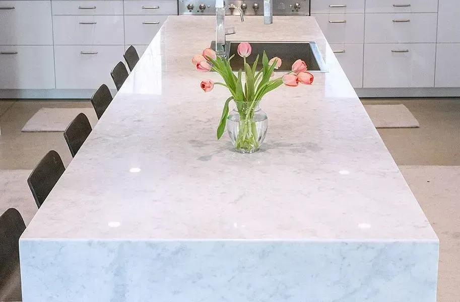 White marble kitchen island with pink tulips, sink, and gray chairs.
