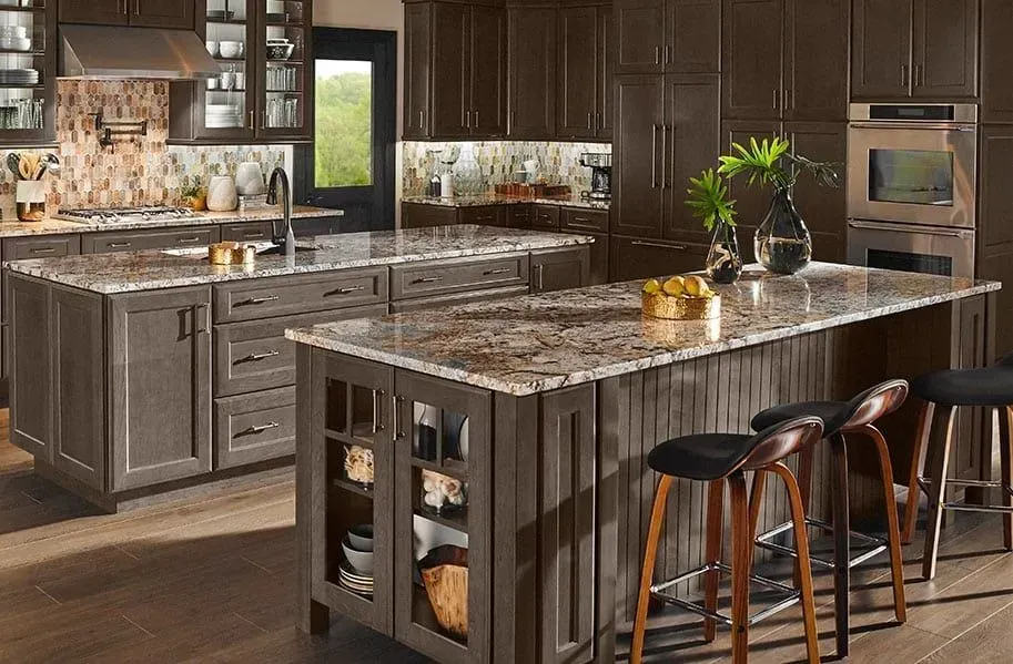Modern kitchen with dark wood cabinets, granite countertops, and two islands; bar stools at one island.