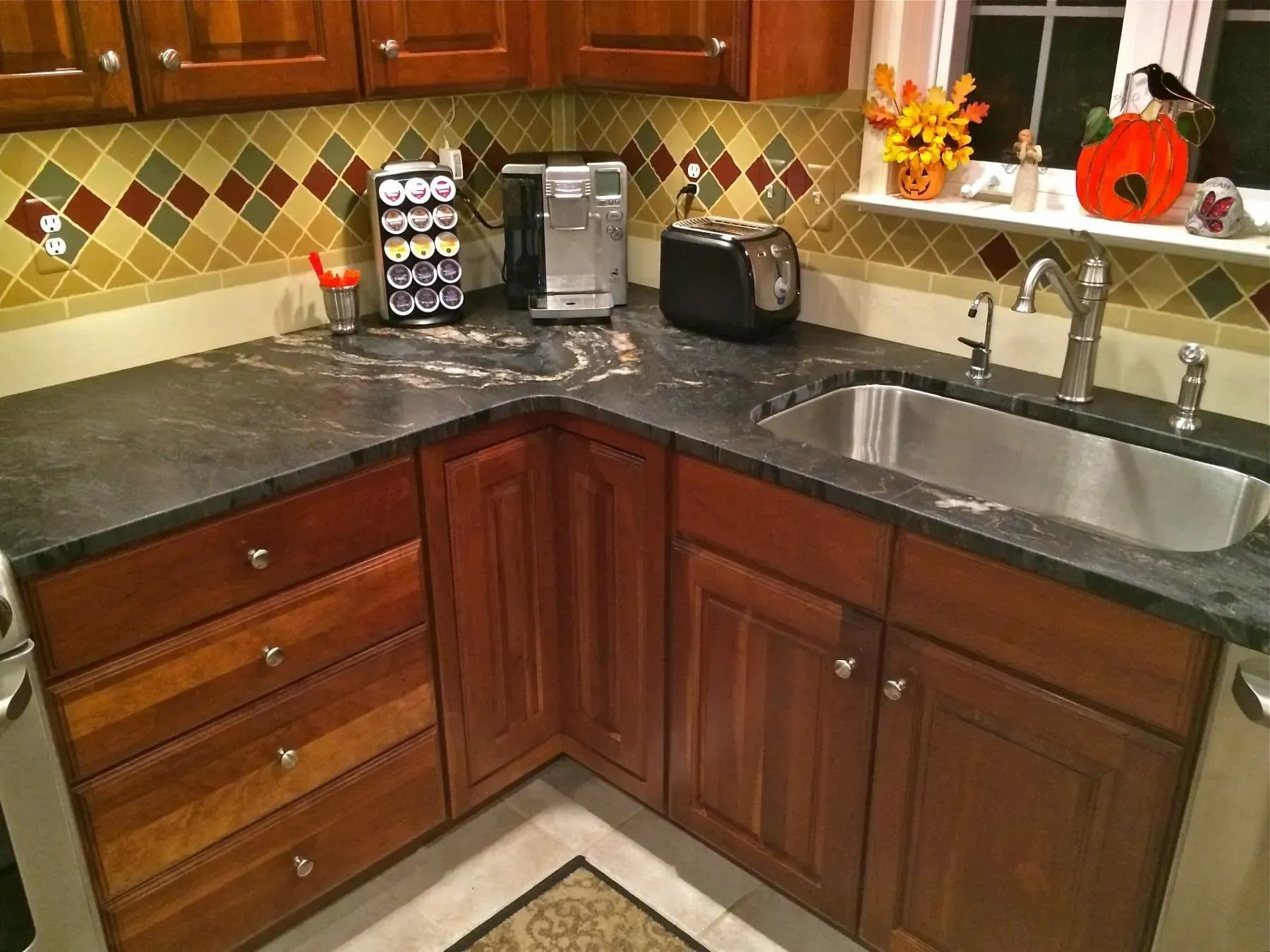 Kitchen with dark countertop, brown cabinets, and a stainless steel sink, toaster, and coffee maker.