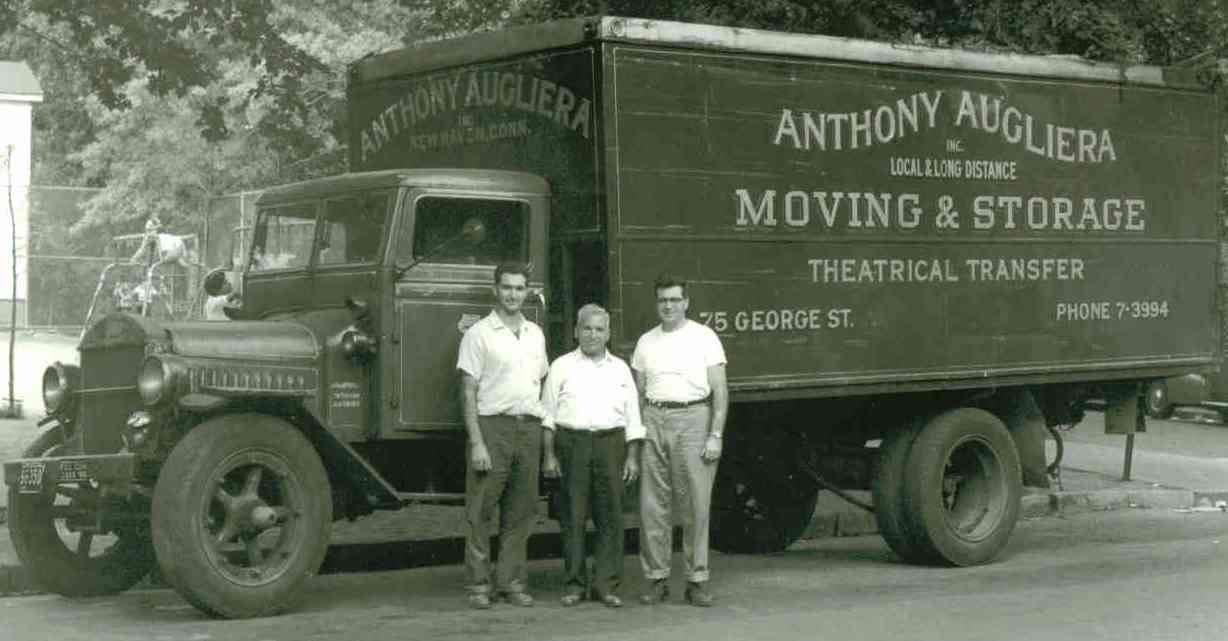 Three men are standing in front of a moving and storage truck.