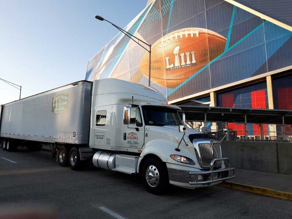 A white semi truck is parked in front of a building with a football on it.