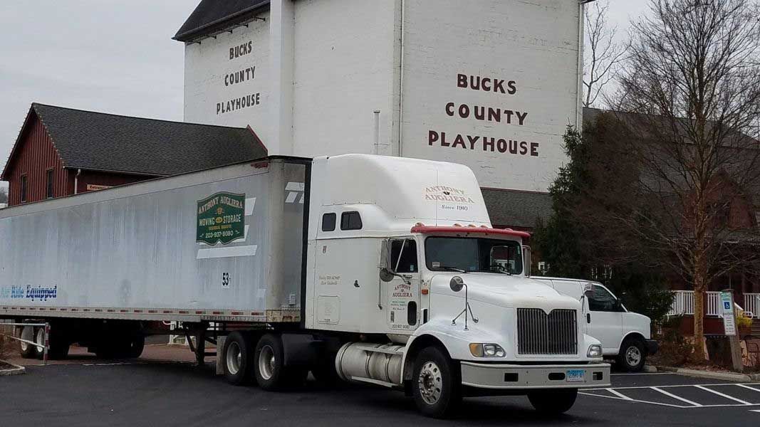 A white semi truck is parked in front of a building that says bucks county flat hobie.