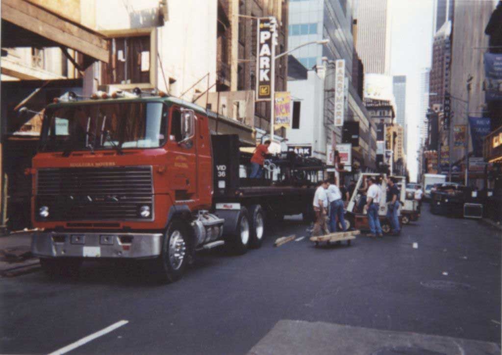 A large red truck is driving down a city street in front of a park sign