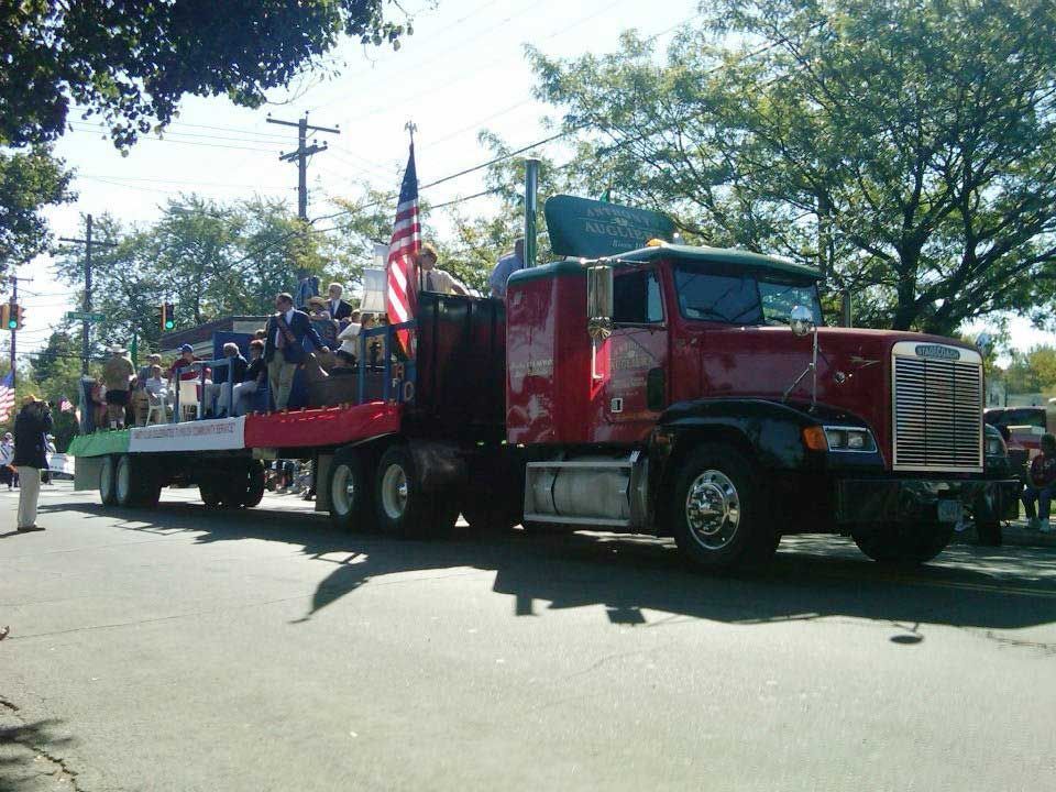 A red semi truck is pulling a float down a street