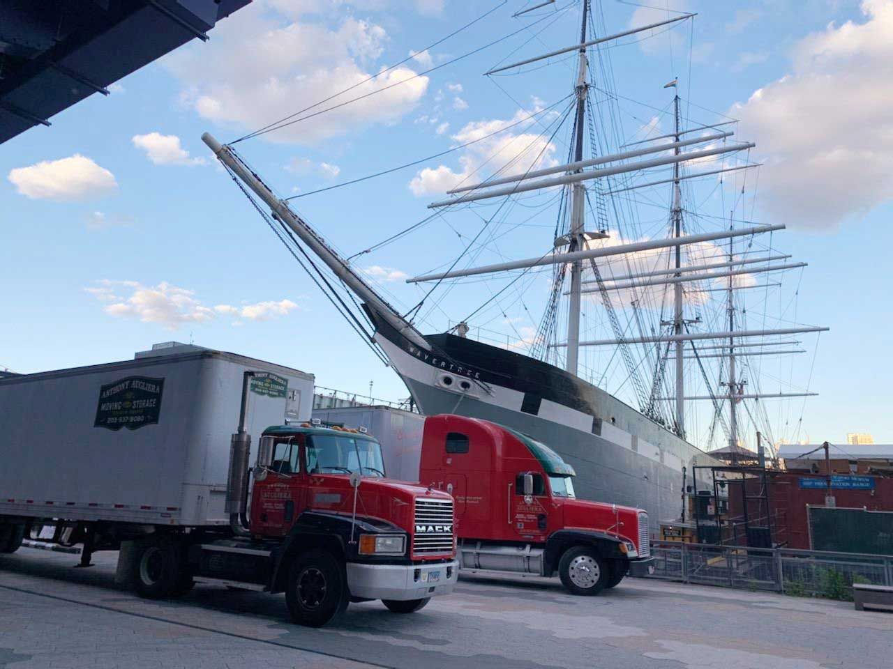 Two trucks are parked in front of a large ship.