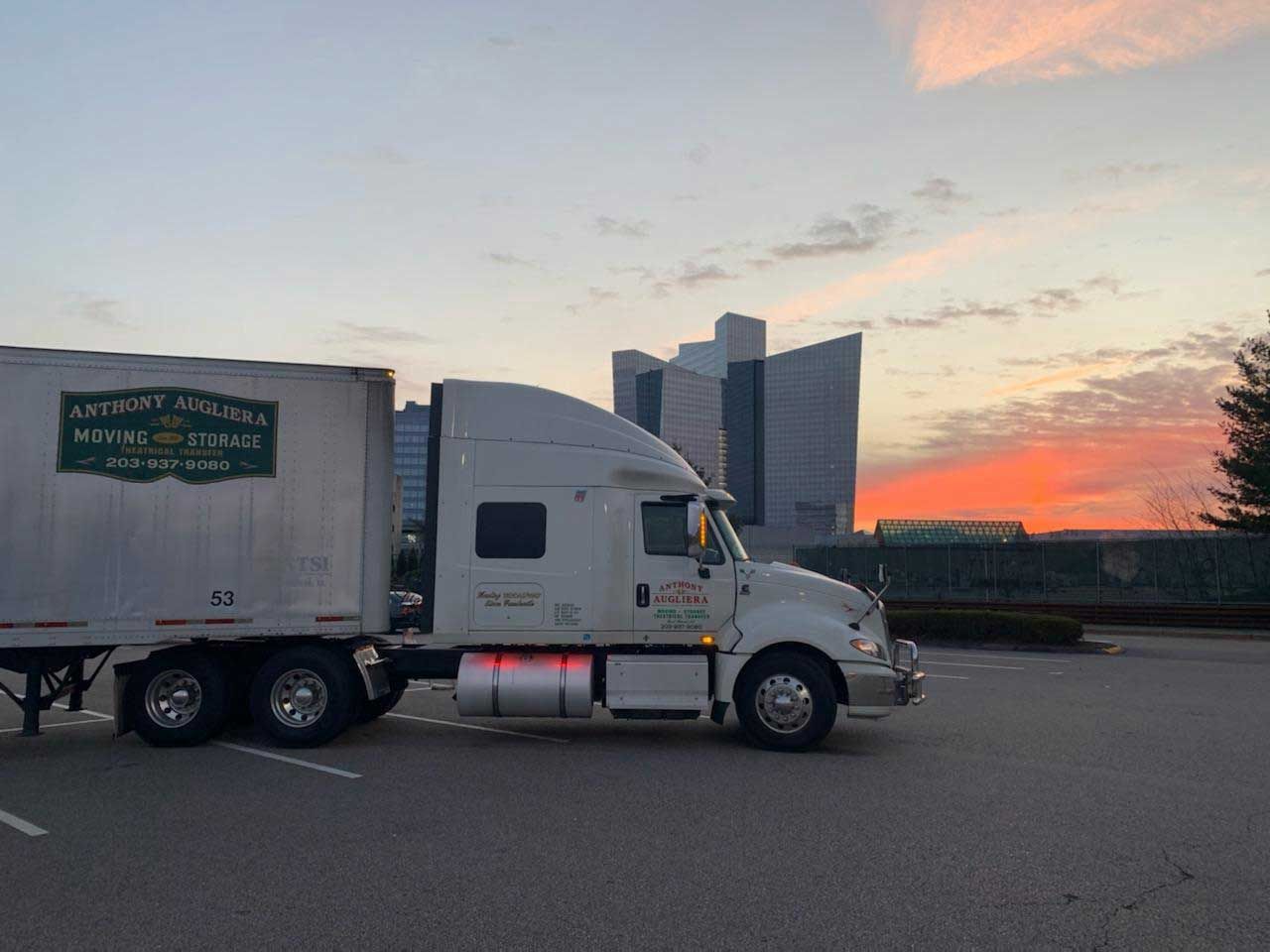 A semi truck is parked in a parking lot with a sunset in the background.