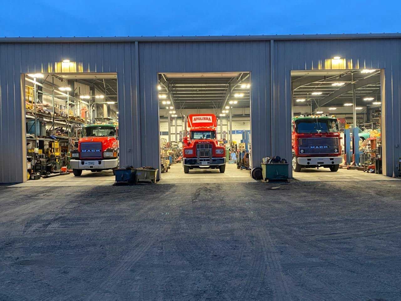 Three trucks are parked in a garage with their doors open.