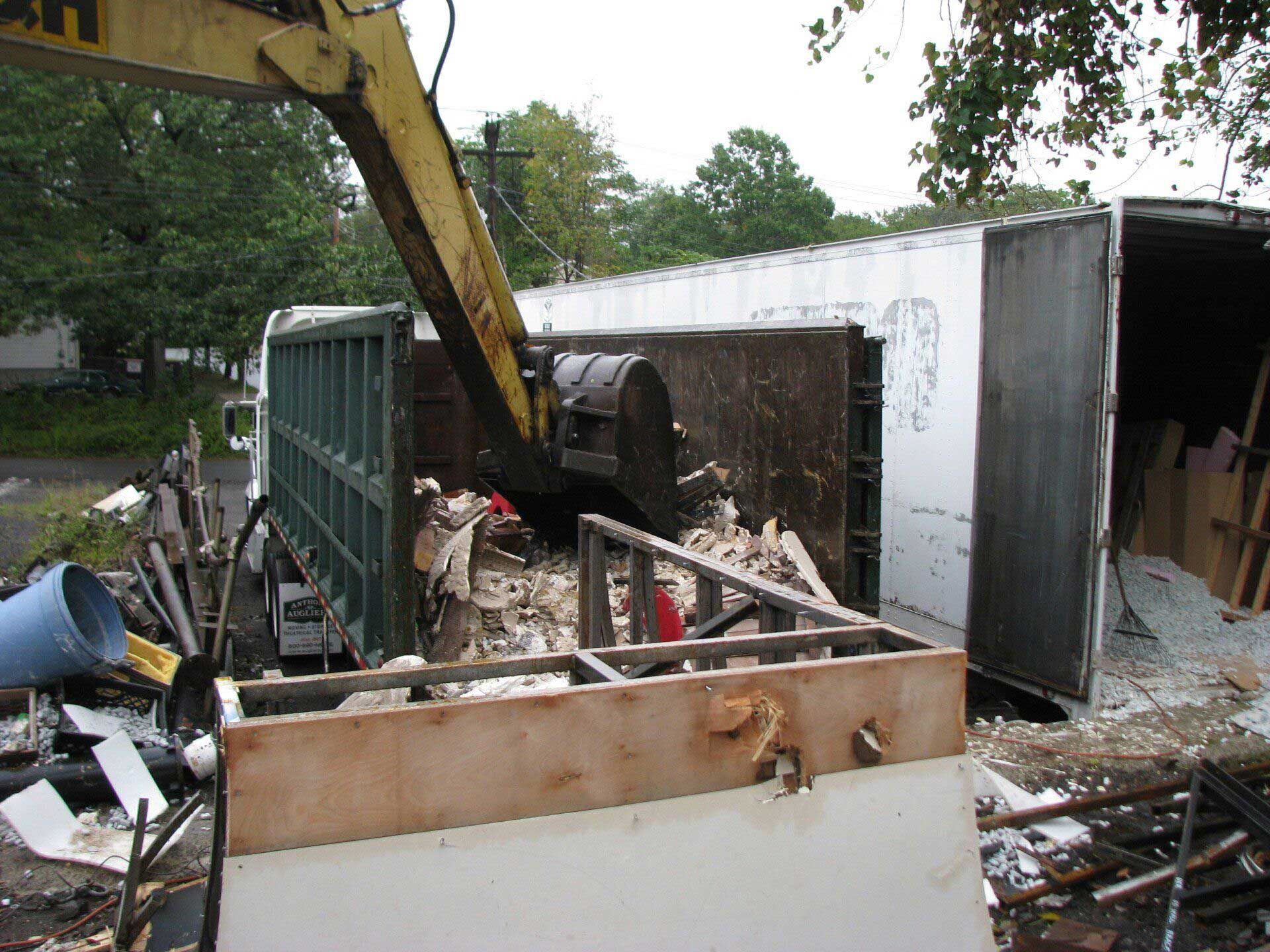 A yellow excavator is digging into a pile of rubble