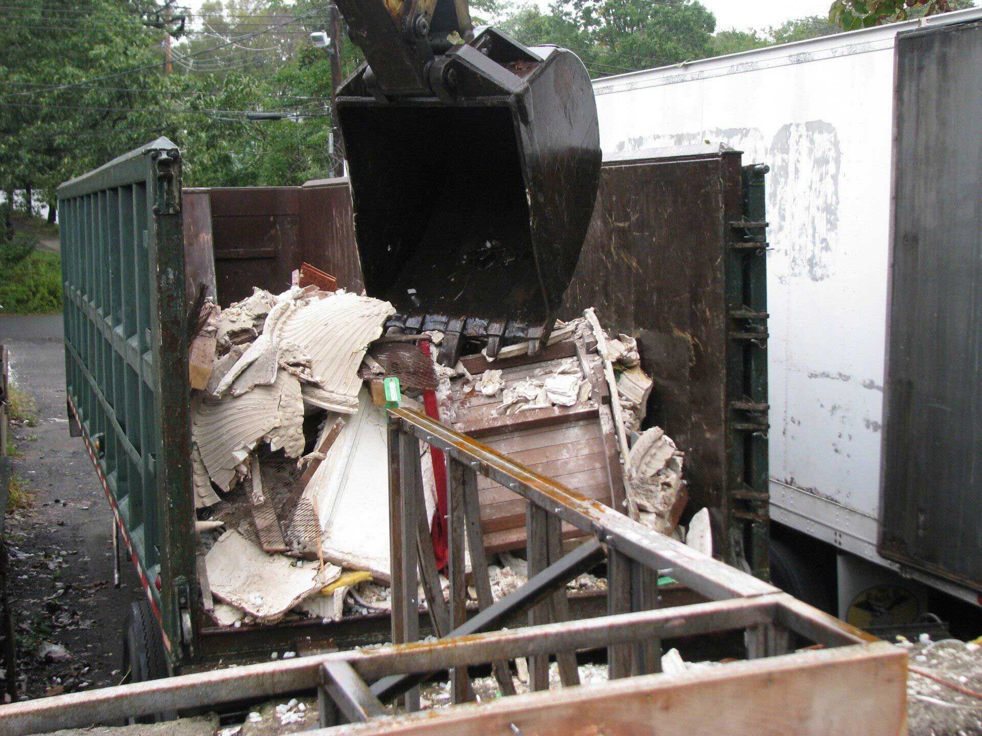 A dumpster filled with junk is being loaded by a crane