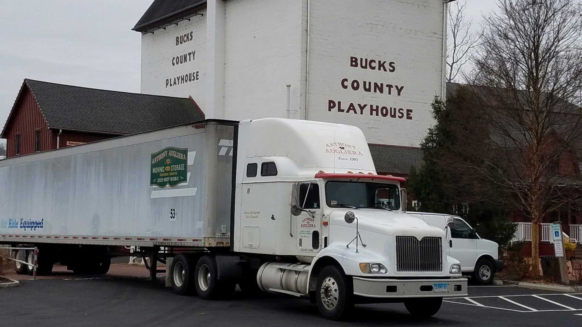 A white semi truck is parked in front of a building that says bucks county playhouse