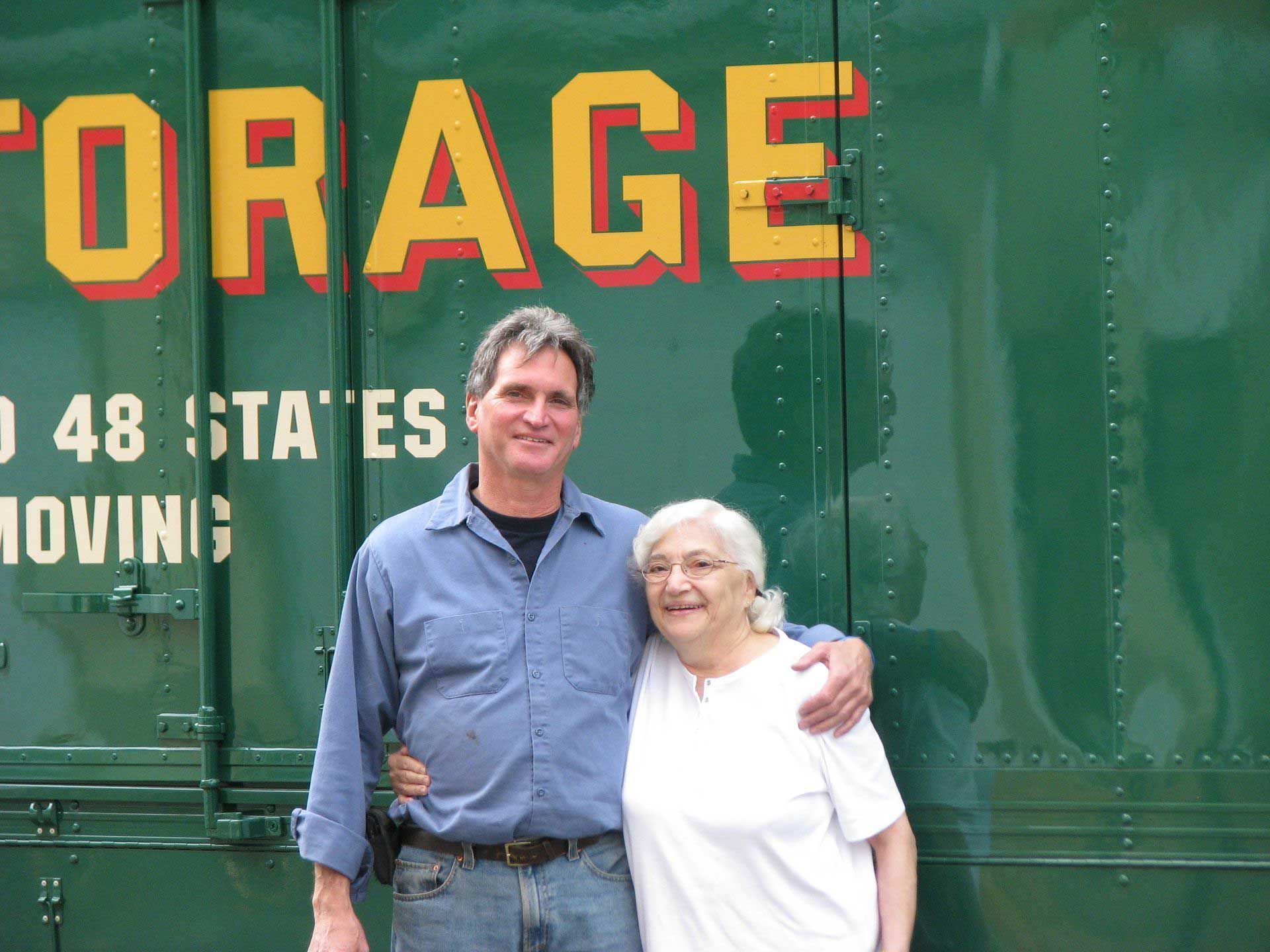 A man and woman are posing in front of a storage truck
