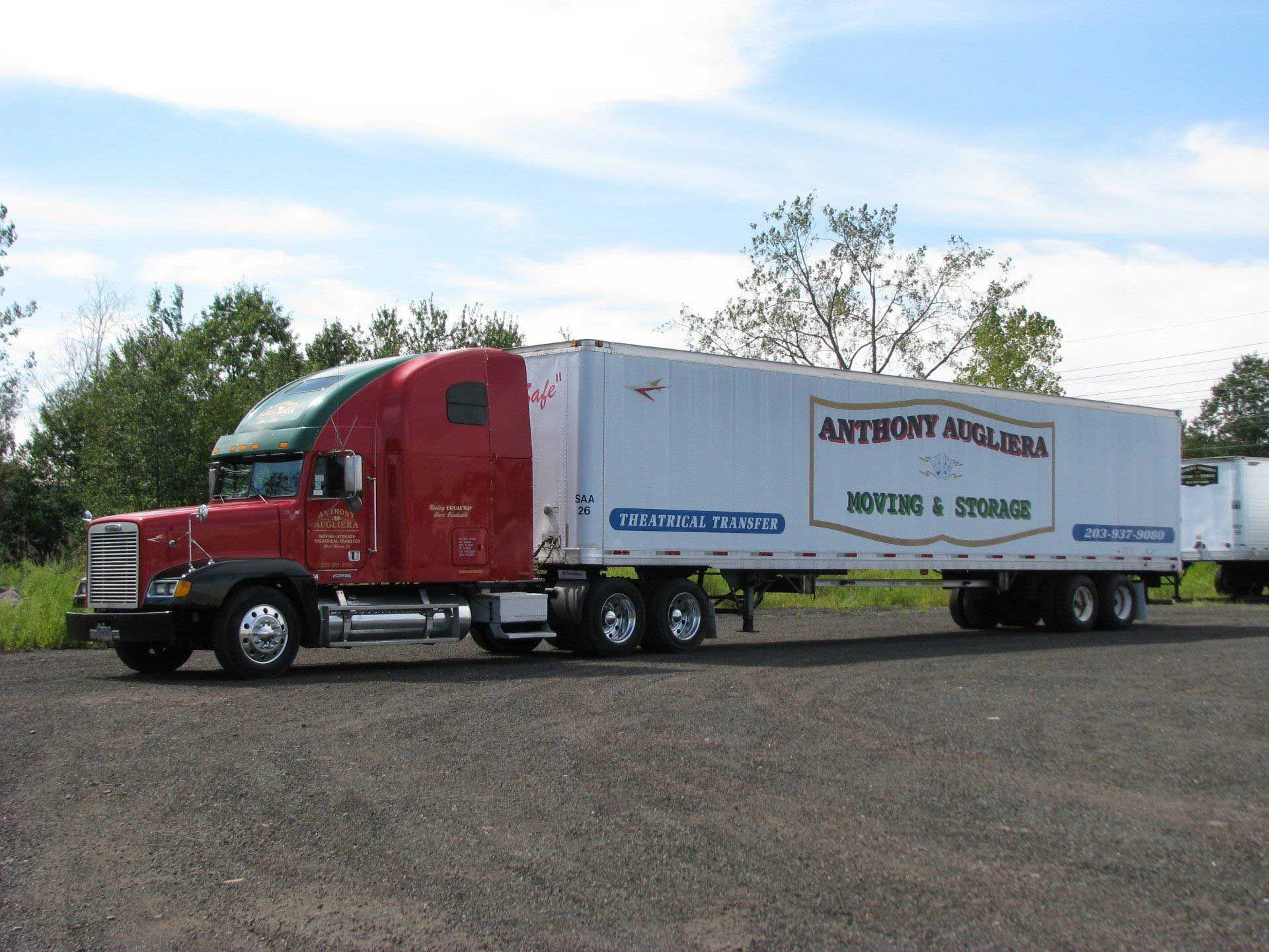 A red semi truck is parked next to a white trailer that says moving & storage