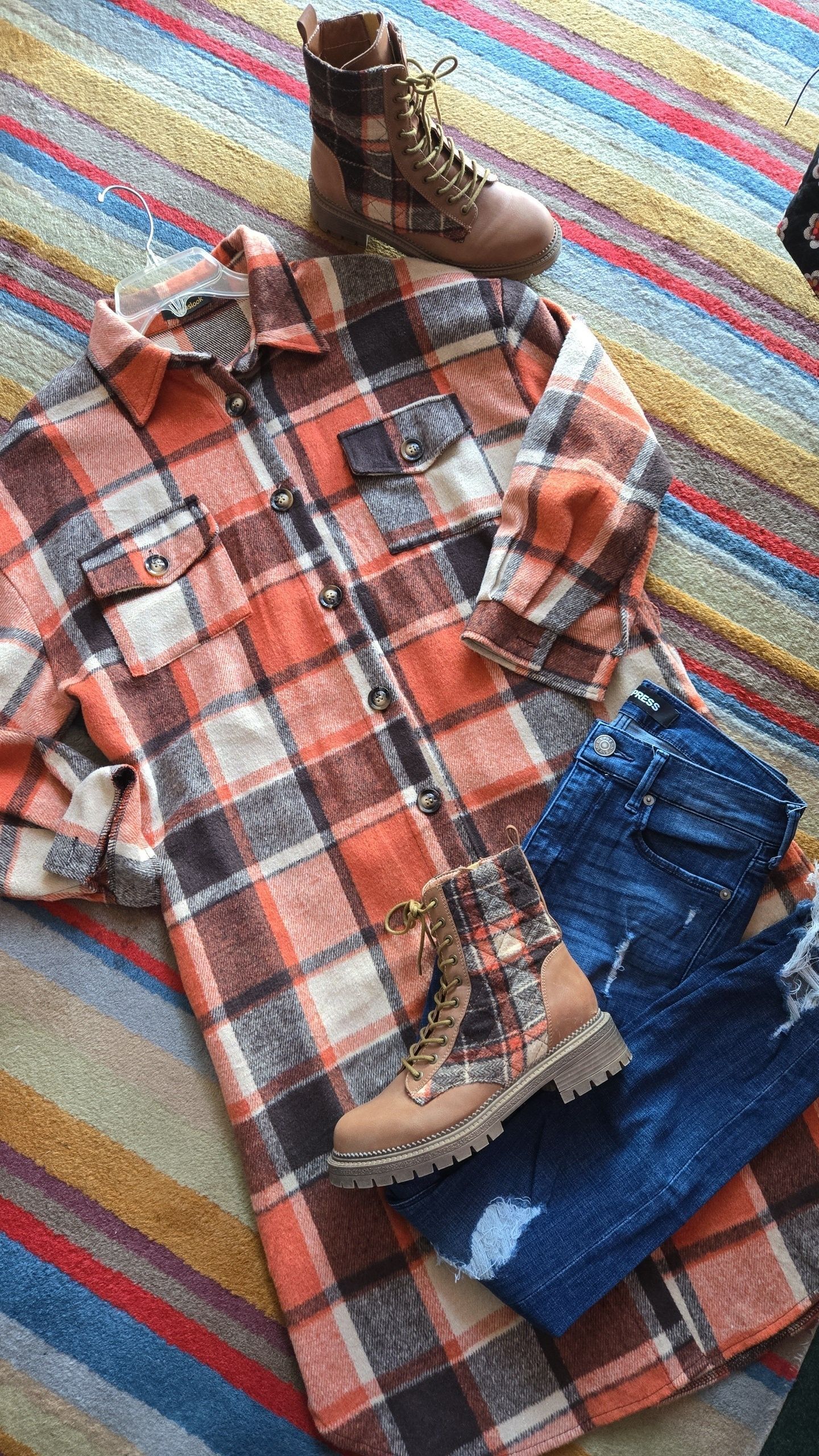 Outfit flat lay: Plaid shirt, blue jeans, and tan plaid boots on a striped rug.