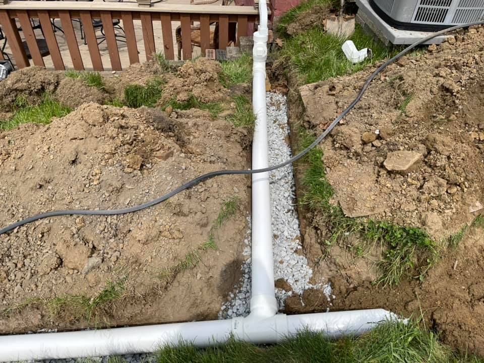A drain pipe is being installed in the dirt next to a fence.